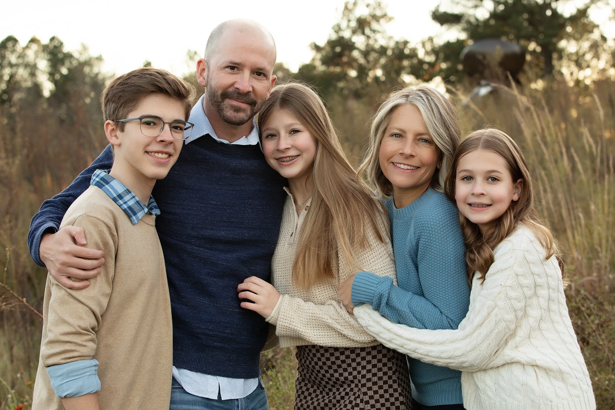 A family of six: a father, mother, three daughters, and a son, posing together outdoors during fall.
