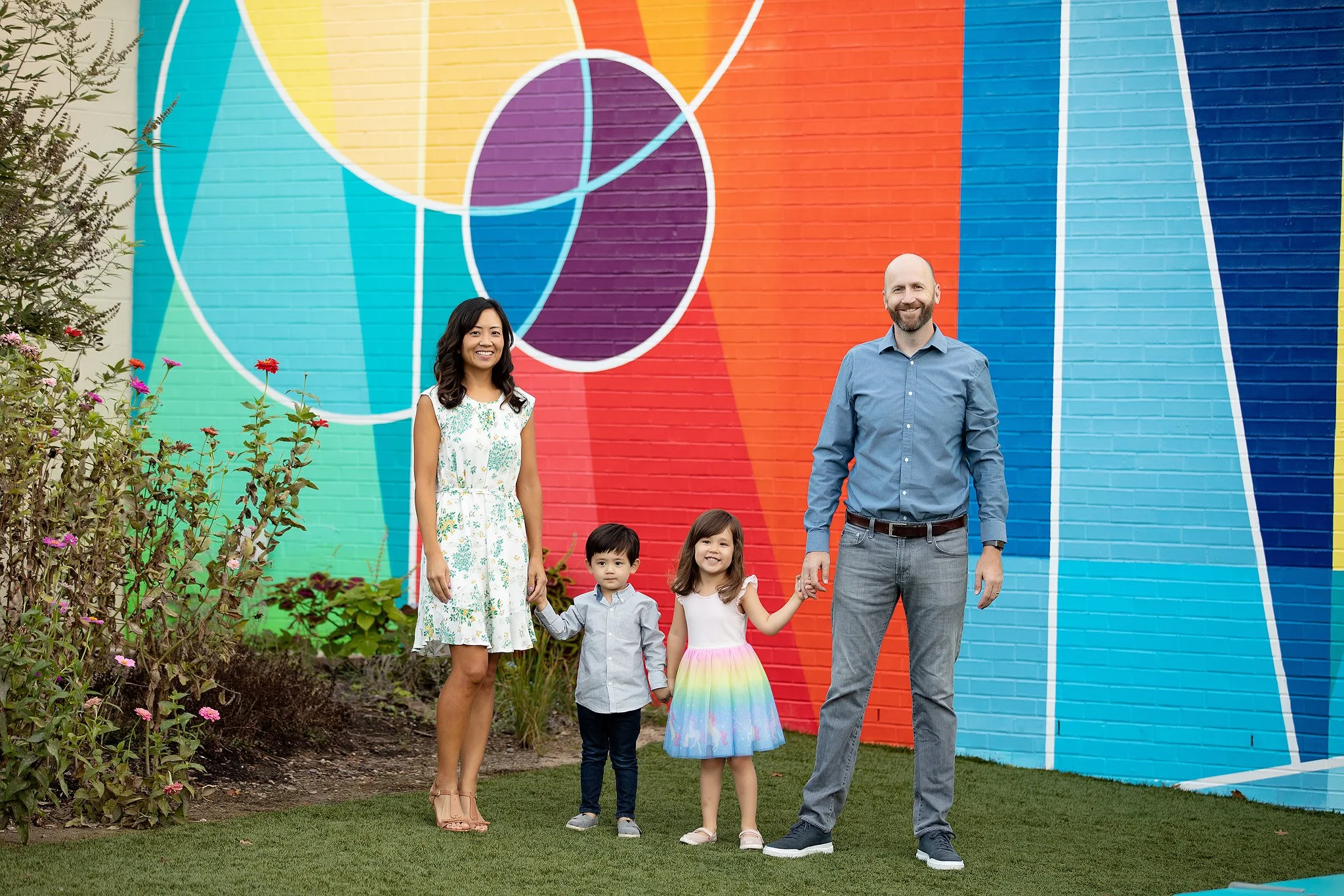 Family standing outdoors in front of colorful mural wall holding hands