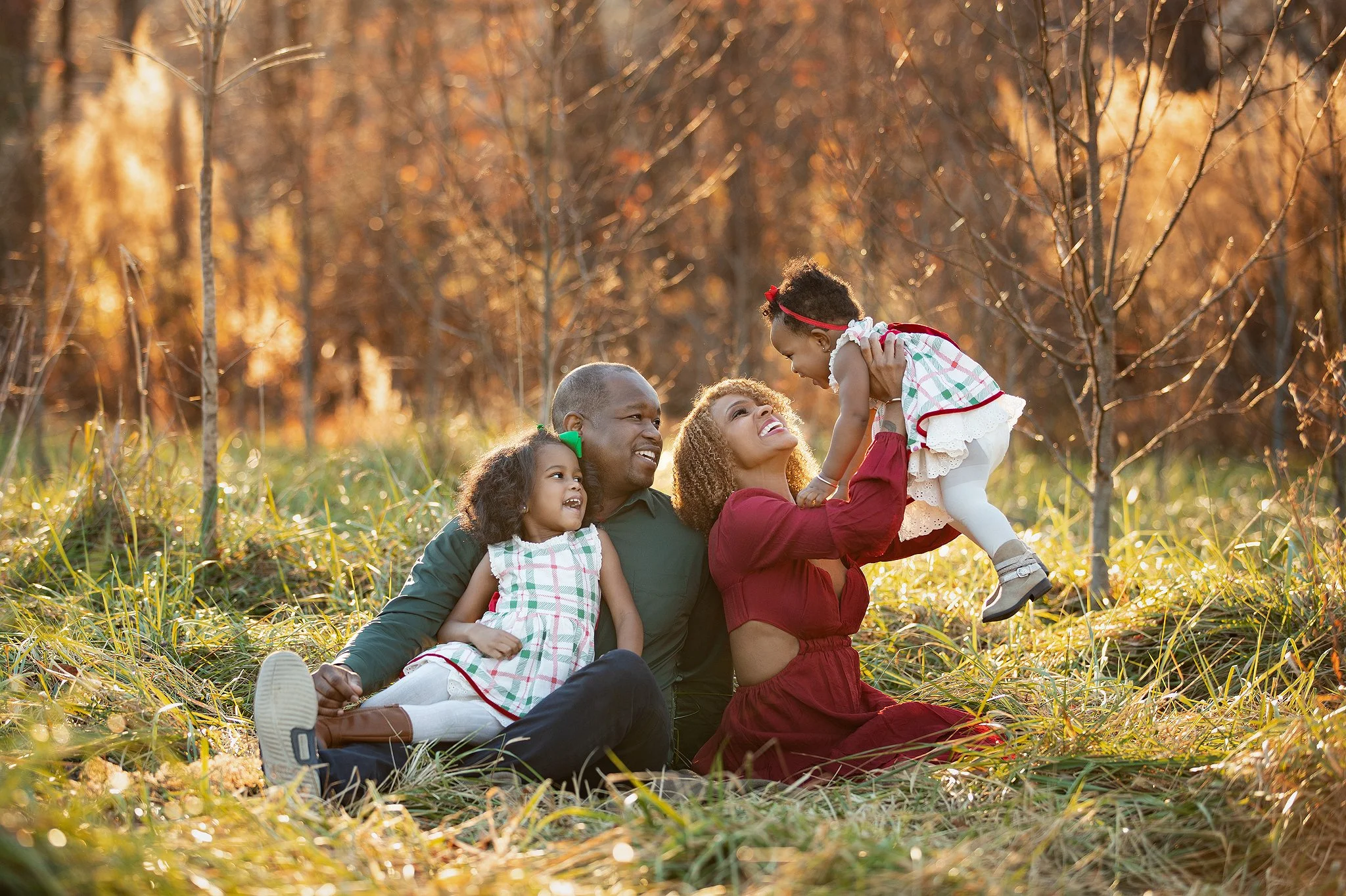 Family of four enjoying autumn in a park with trees and fallen leaves, smiling and playing together outdoors.