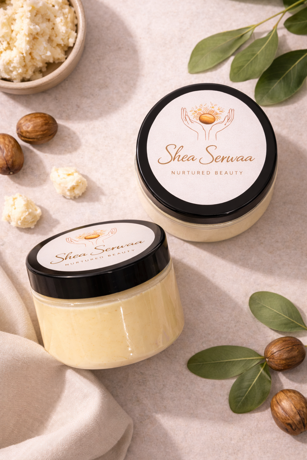 Two jars of Shea Serwaa skincare product with labels reading 'Nurtured Beauty,' surrounded by shea nuts, shea butter, and green leaves on a neutral background.