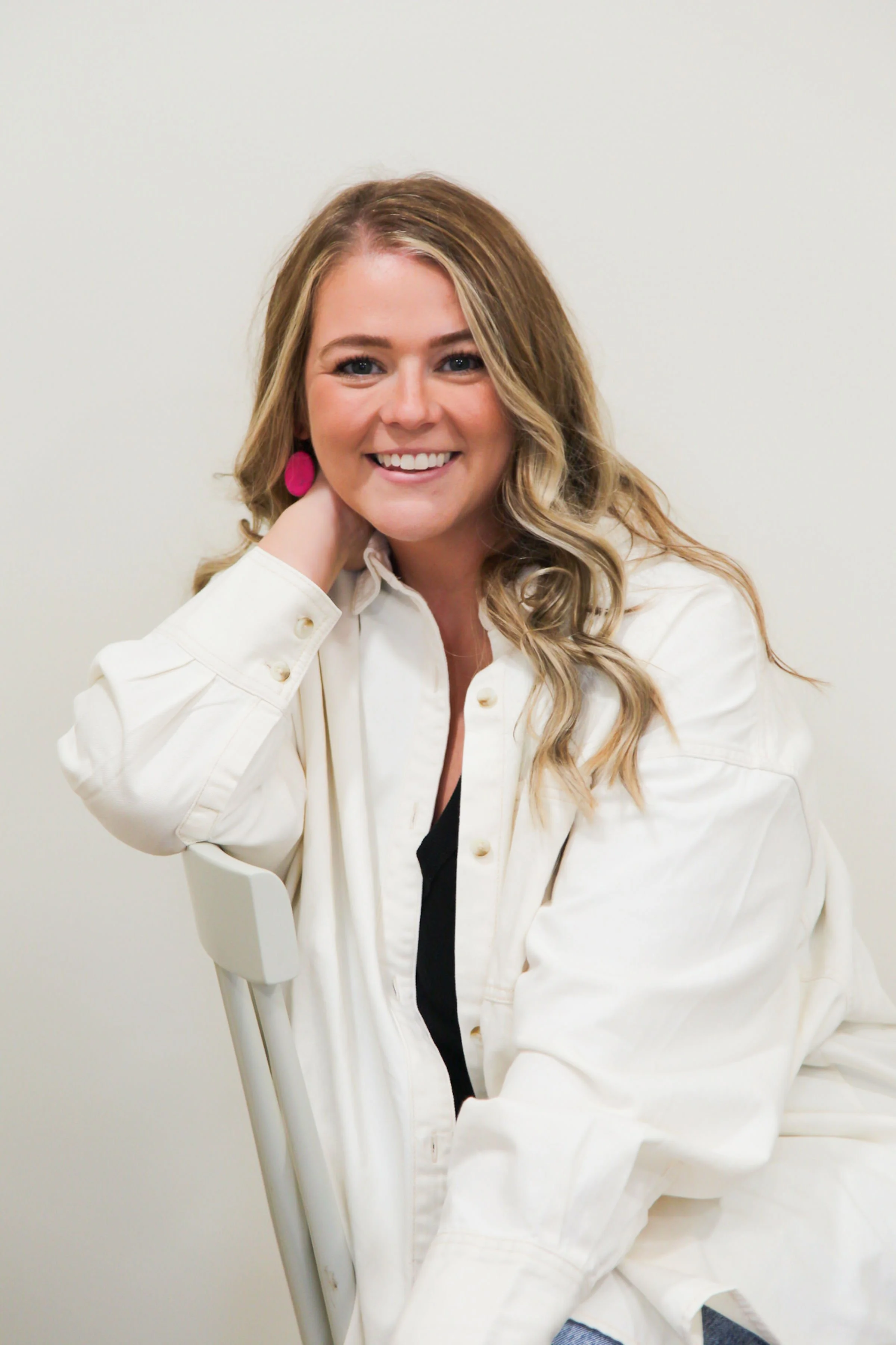 Smiling woman with long blonde hair wearing a white jacket and pink earrings
