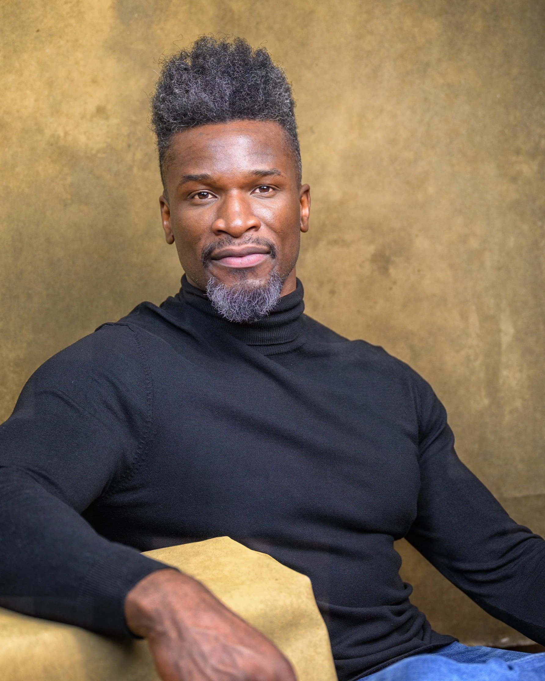 Professional traditional portrait of a seated man photographed in a studio with a textured background.