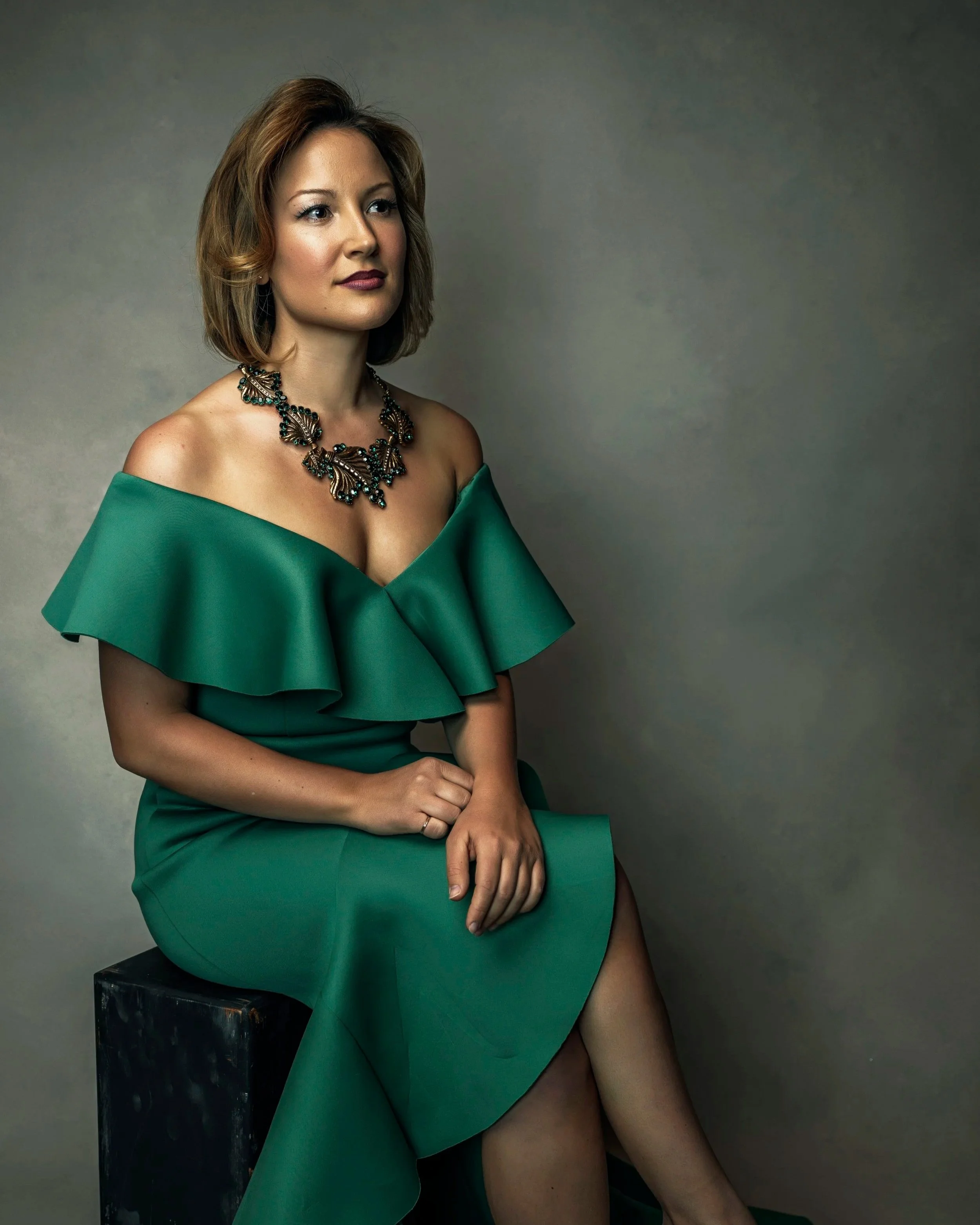 Elegant seated portrait of a woman in a green dress photographed with soft studio lighting.
