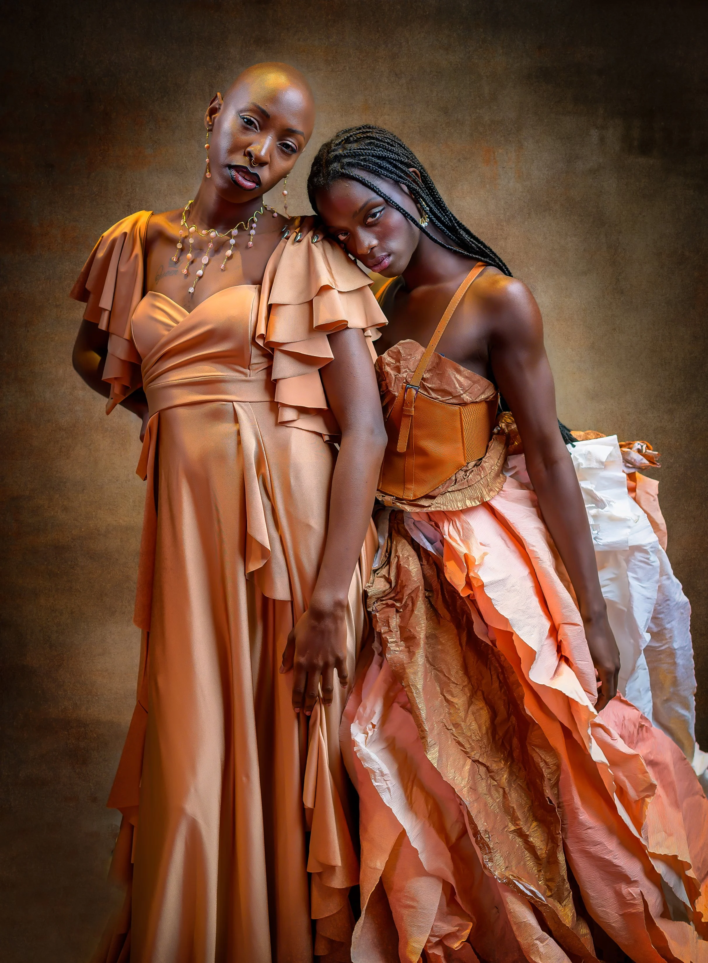 Fine art portrait of two women in elegant gowns embracing in a painterly studio portrait.