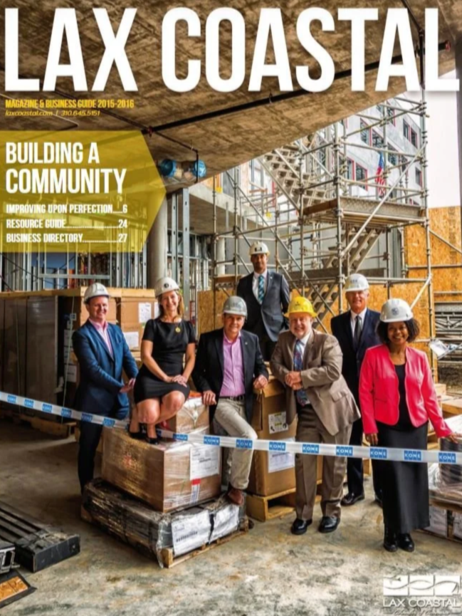 A group of diverse professionals, including men and women in business attire and construction helmets, standing inside a building under construction with scaffolding and unfinished walls, celebrating a milestone with some holding shovels.