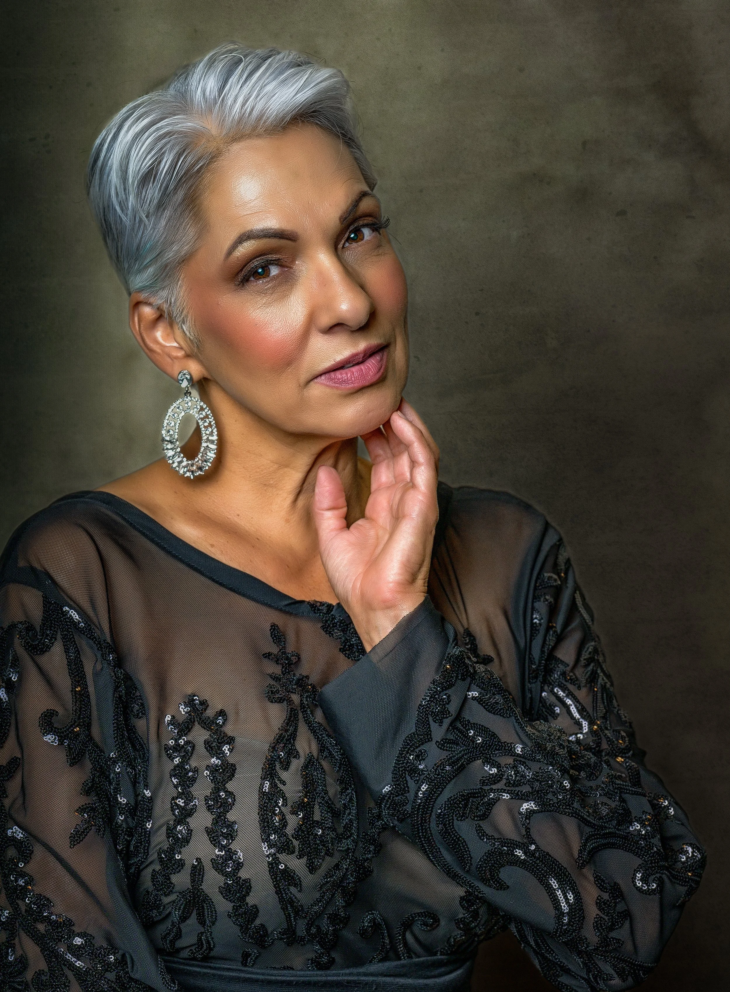 Professional portrait of a woman with silver hair wearing statement earrings and a textured black top, demonstrating how accessories can complement a portrait without distracting from the subject.