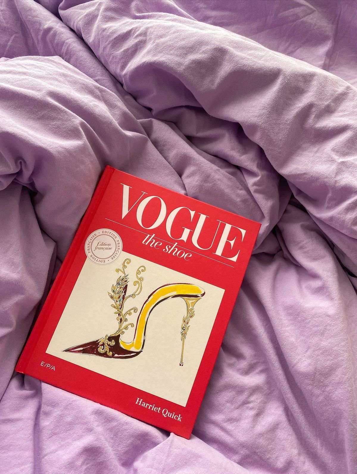 A book titled 'Vogue the shoe' by Harriet Quick resting on purple Bedding.