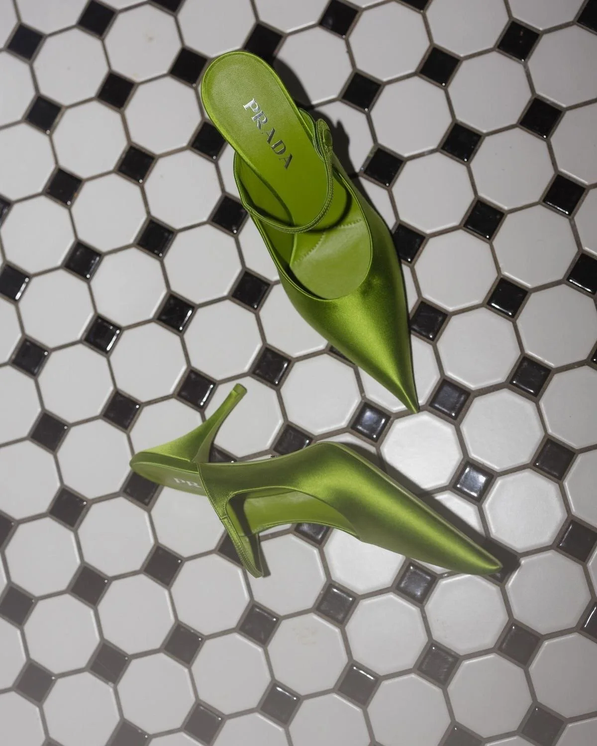 Two green Prada high-heeled shoes placed on a black and white hexagonal tiled floor.