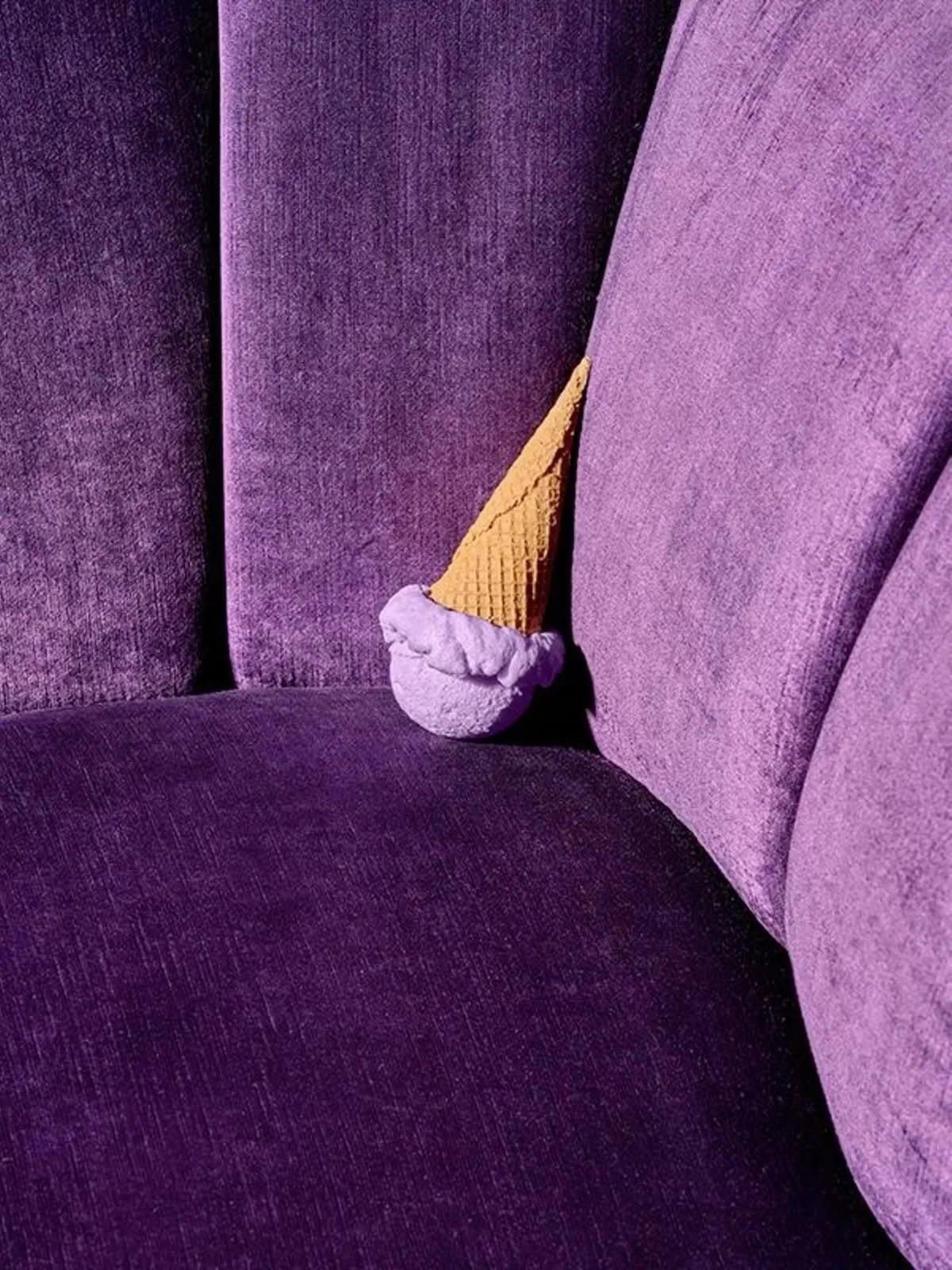 A purple velvet sofa holding an ice cream cone with purple ice cream and a waffle cone, positioned to look like a face.