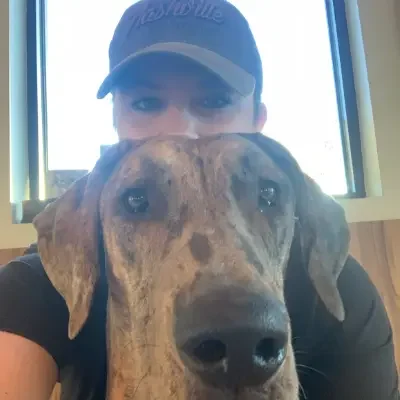 Person wearing a baseball cap taking a selfie with a large dog.