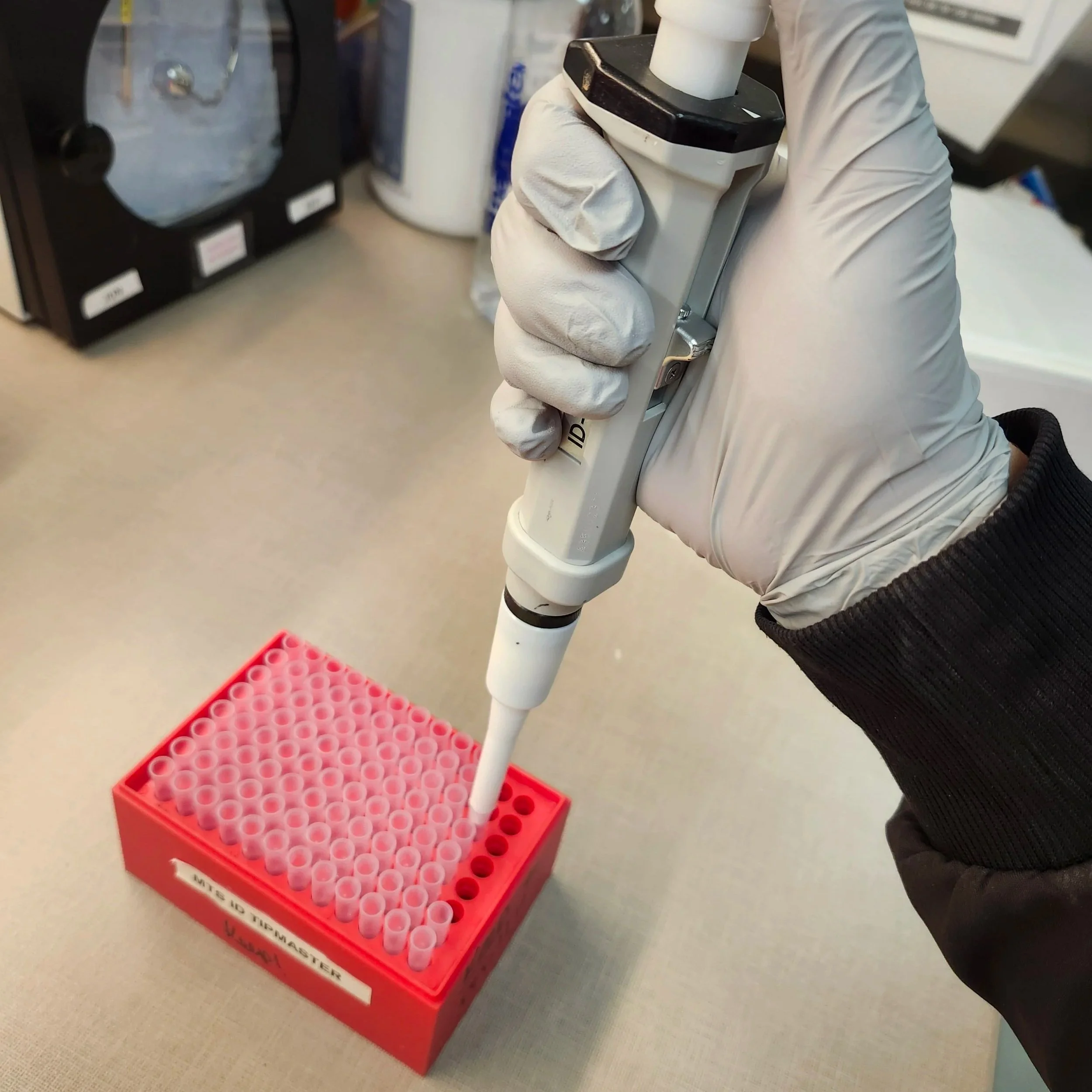 Image of a person using a pipette over laboratory sample tubes.