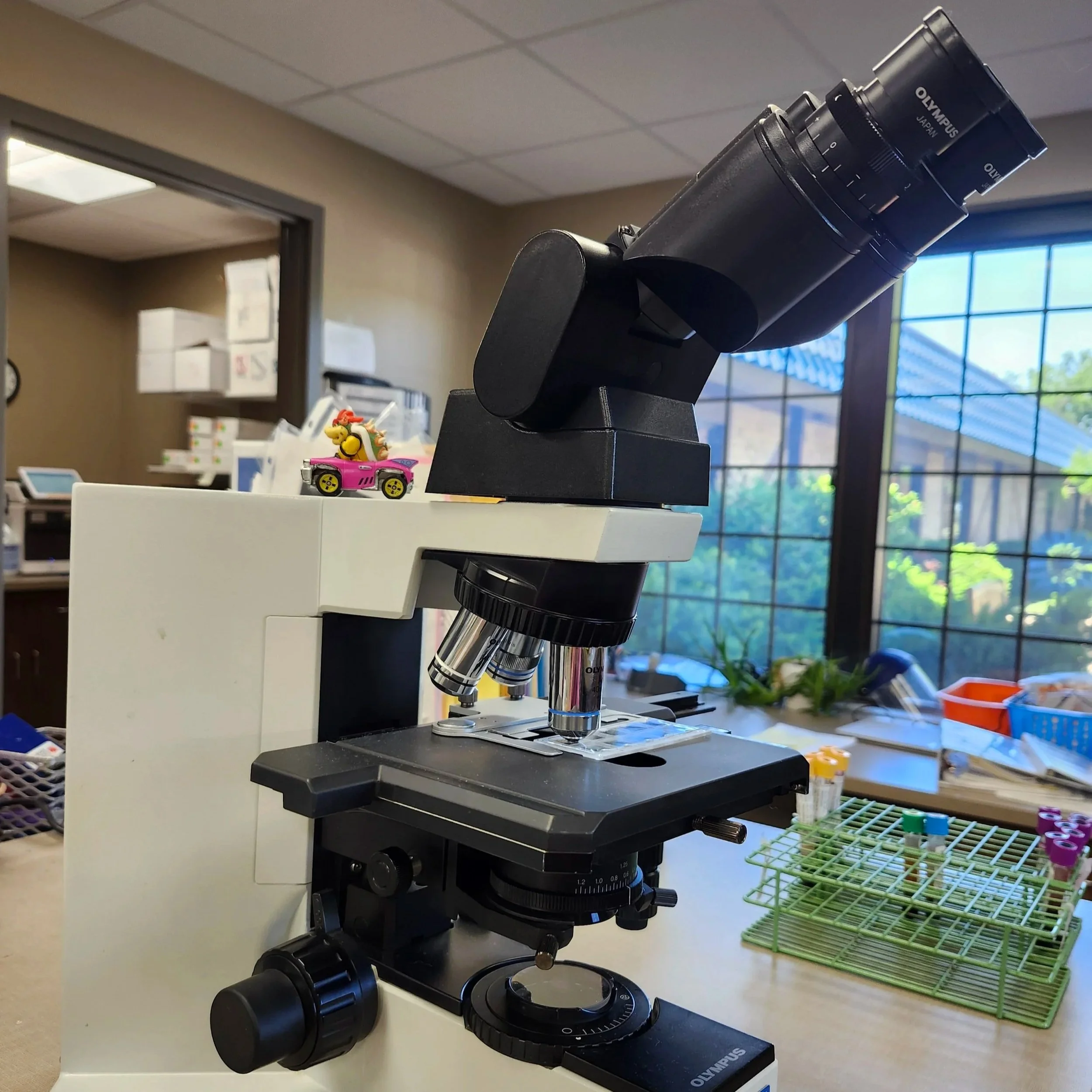 Image of a binocular microscope adjacent to sample vials being stored in a rack.