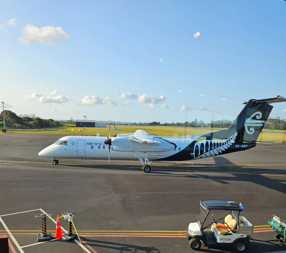 A small aircraft on the tarmac at an airport, with a golf cart nearby and a blue sky with scattered clouds in the background.