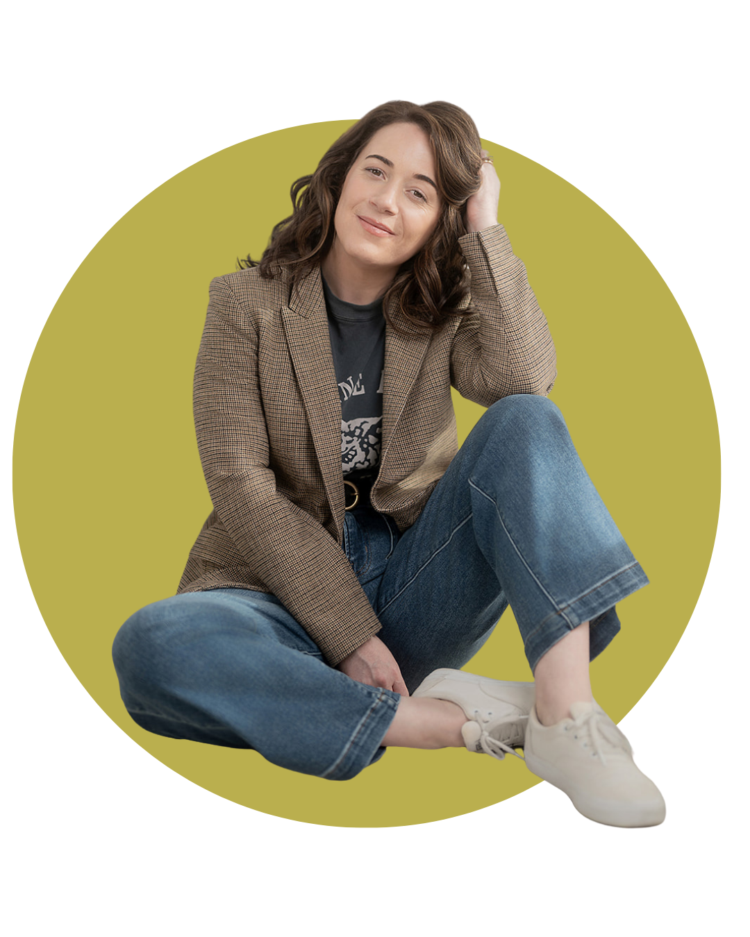 Brigitte Boots sitting on the floor with a yellow background, wearing a blazer, graphic t-shirt, jeans, and white sneakers, smiling gently.
