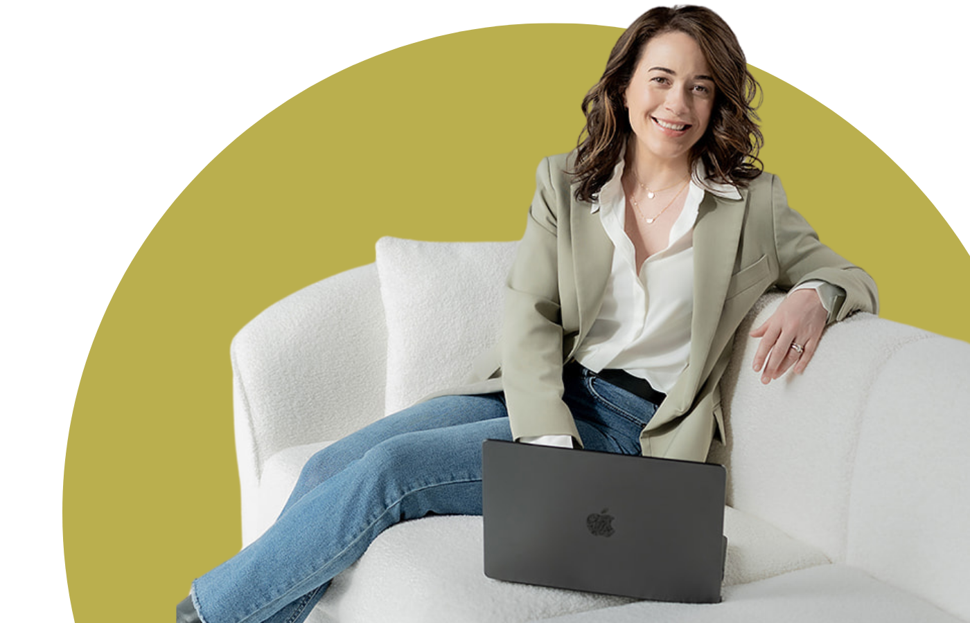 Brigitte Boots sitting on a white sofa with a laptop on her lap, smiling at the camera, in a casual and professional setting.