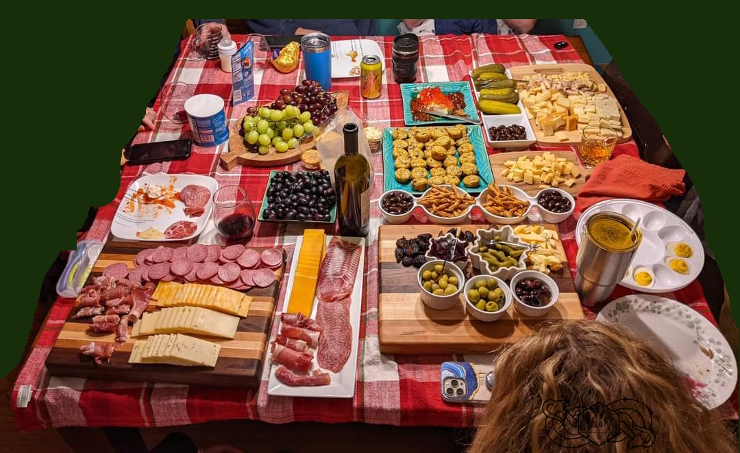 Table with red and white plaid table cloth covered with charcuterie boards, food, and wine.
