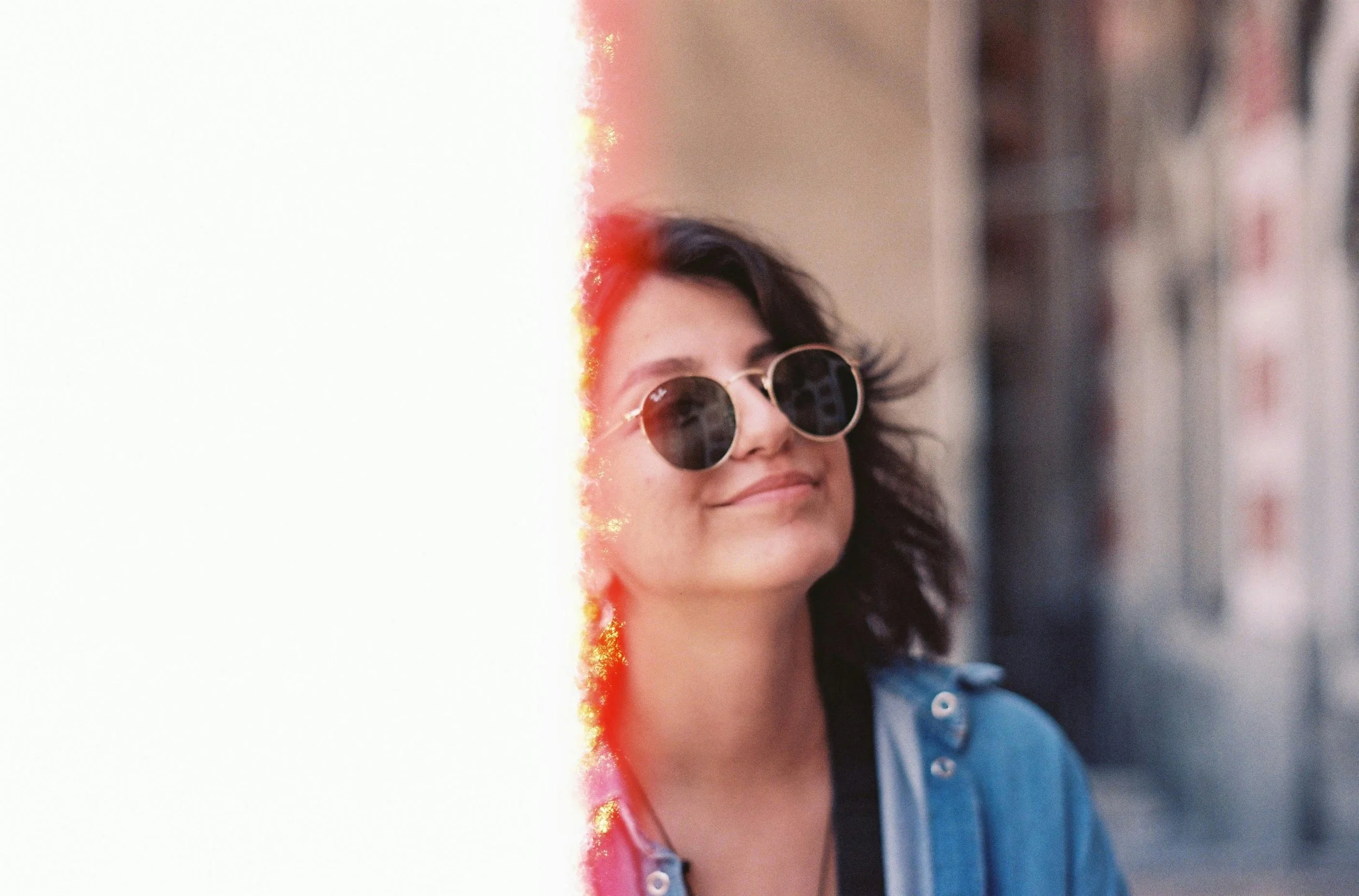 Young woman wearing sunglasses smiling with a blurred background.