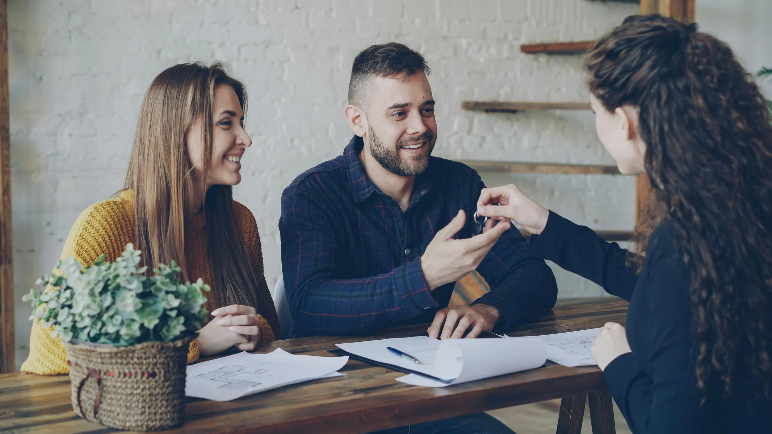 Group of four people sitting at a table, with one person handing a key to another, in an indoor setting.