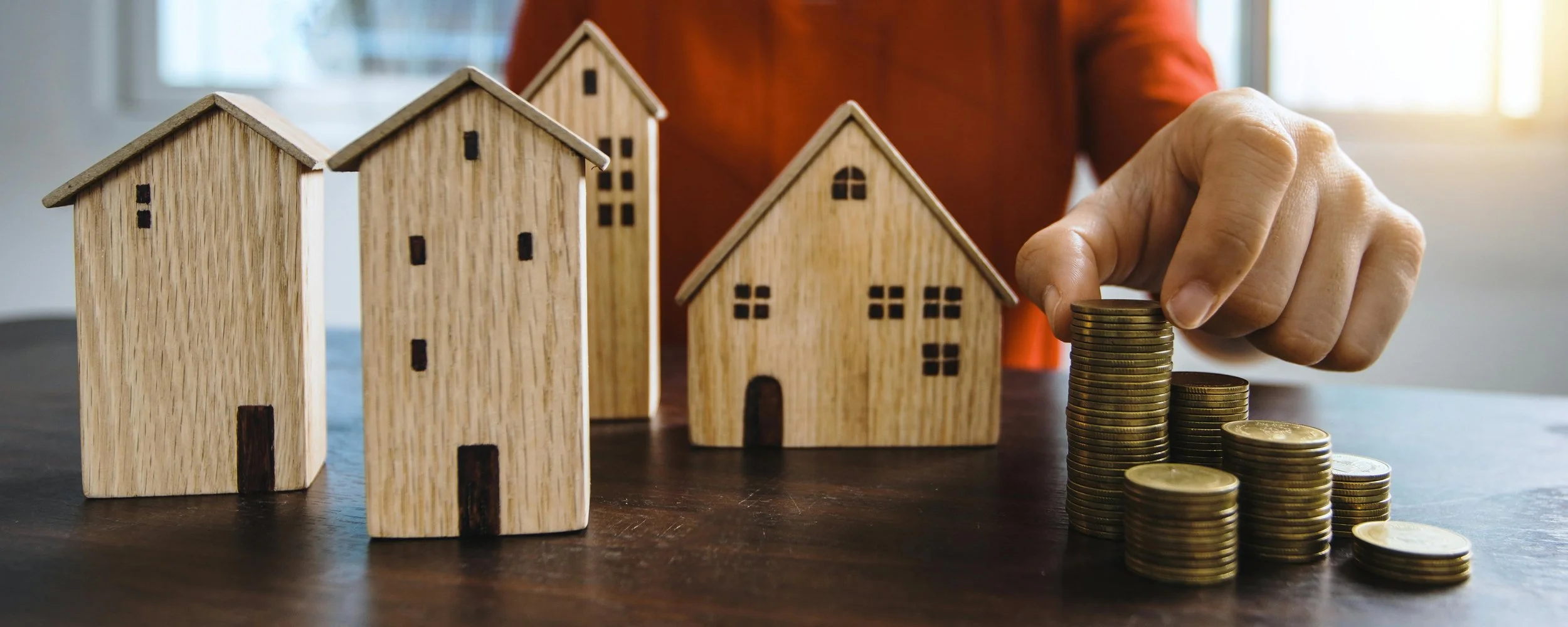 Wooden model houses and a person stacking coins, symbolizing real estate investment or property value.