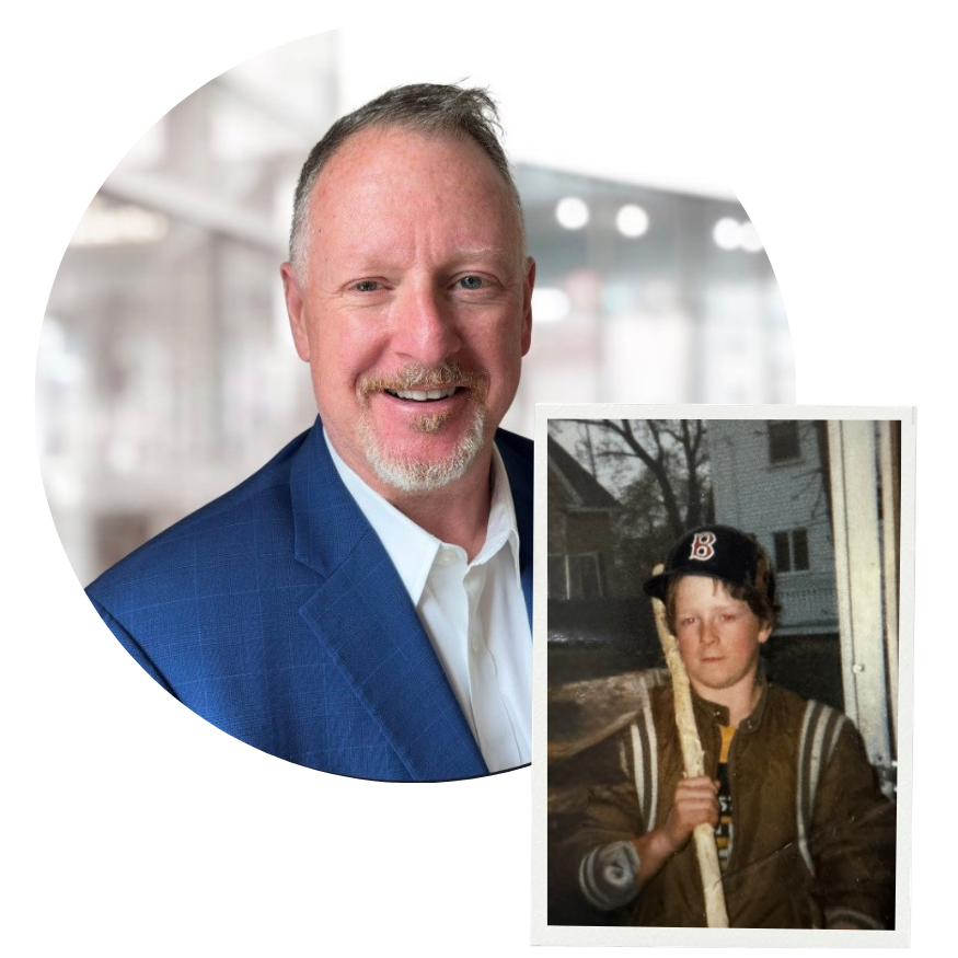 A smiling middle-aged man with short hair and a goatee, wearing a blue suit and white shirt, standing indoors with a blurred modern office background. Overlaid in the corner is a childhood photo of the same man wearing a baseball cap and jacket, holding a stick outdoors.