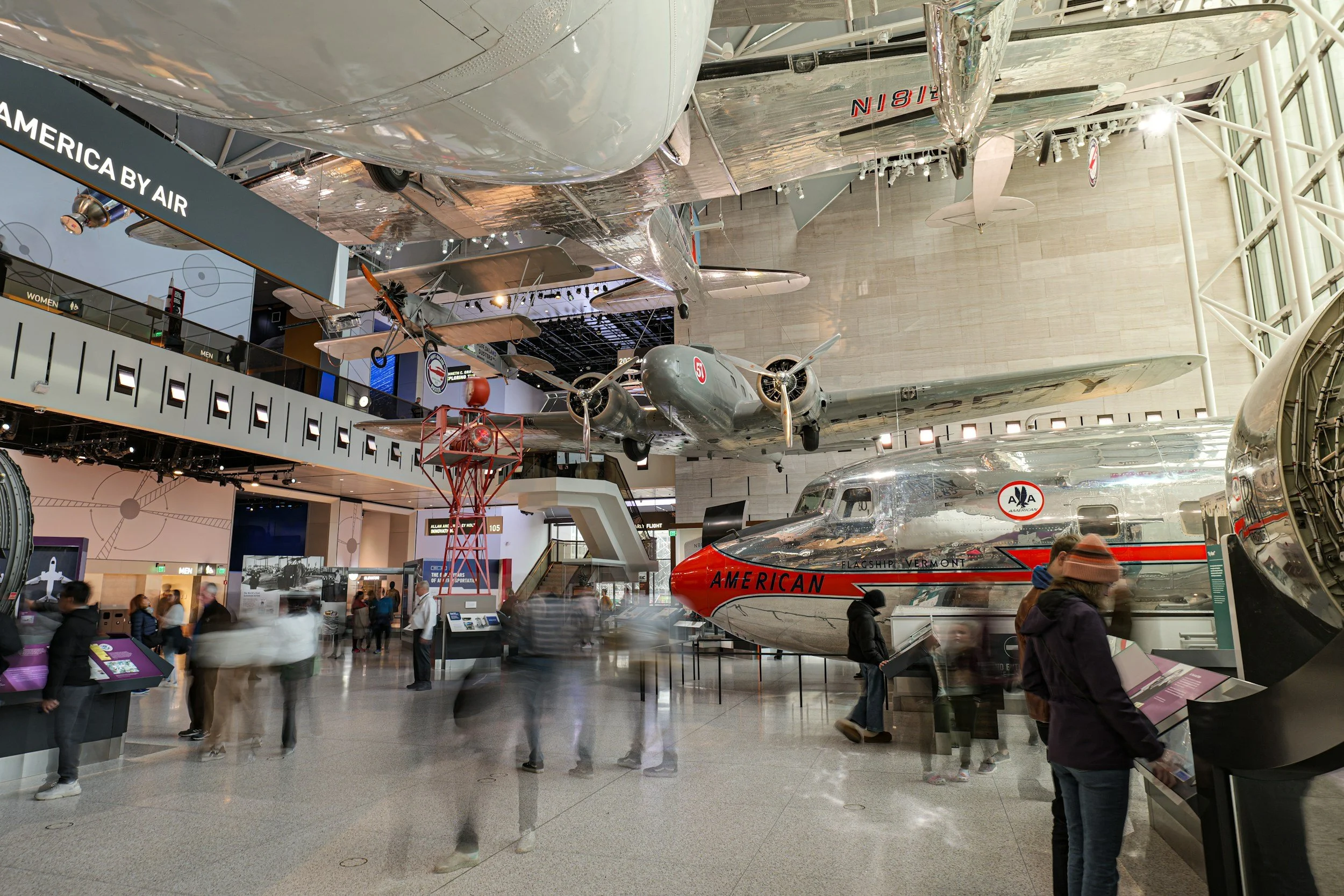 Exhibit of vintage aircrafts displayed indoors at an aviation museum, with visitors walking around and observing.
