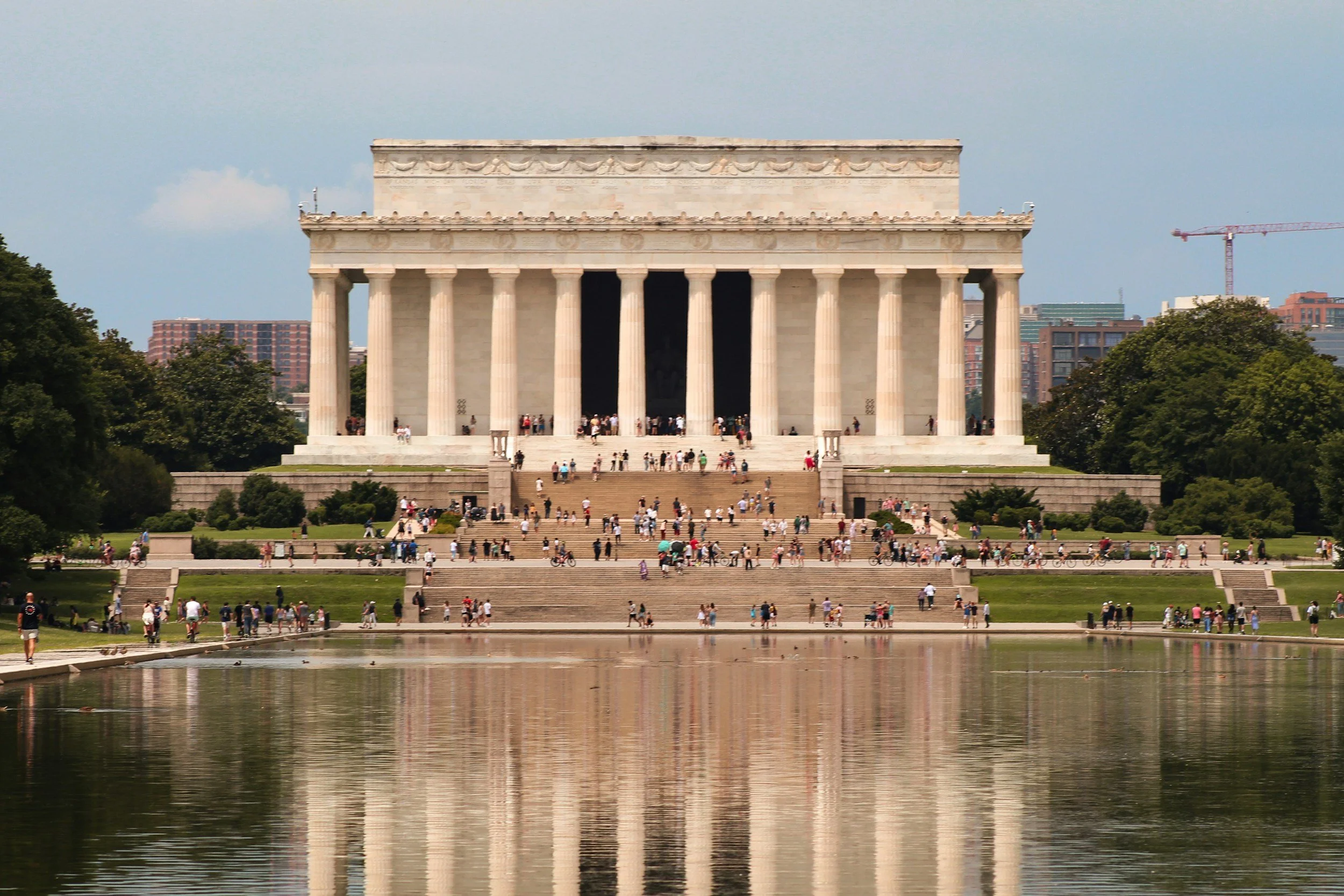 The Lincoln Memorial in Washington, D.C., with a reflecting pool in the foreground, surrounded by trees and a crowded staircase with visitors.