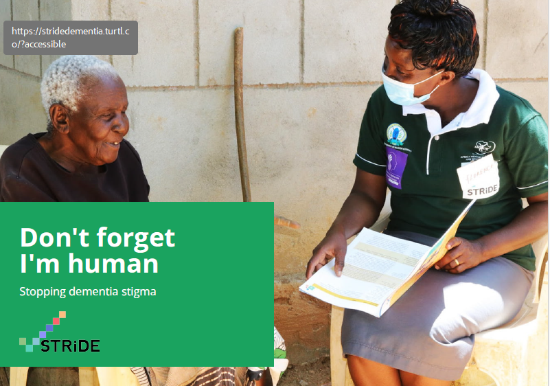 An elderly woman and a healthcare worker sitting outside against a concrete wall, having a conversation. The healthcare worker is holding a booklet and wearing a face mask.
