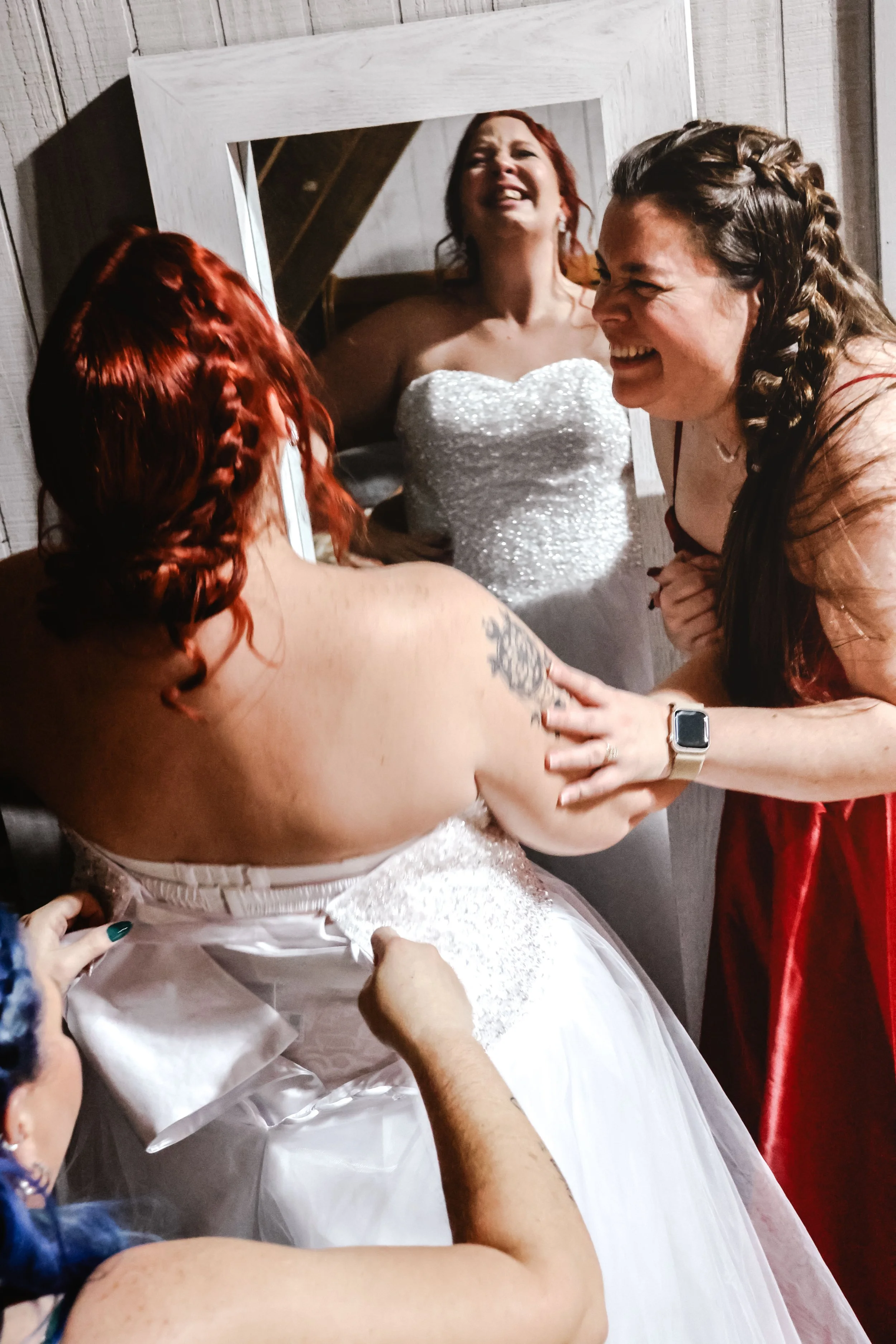 A bride in a white gown smiling as she is surrounded by friends or family in a joyful moment.