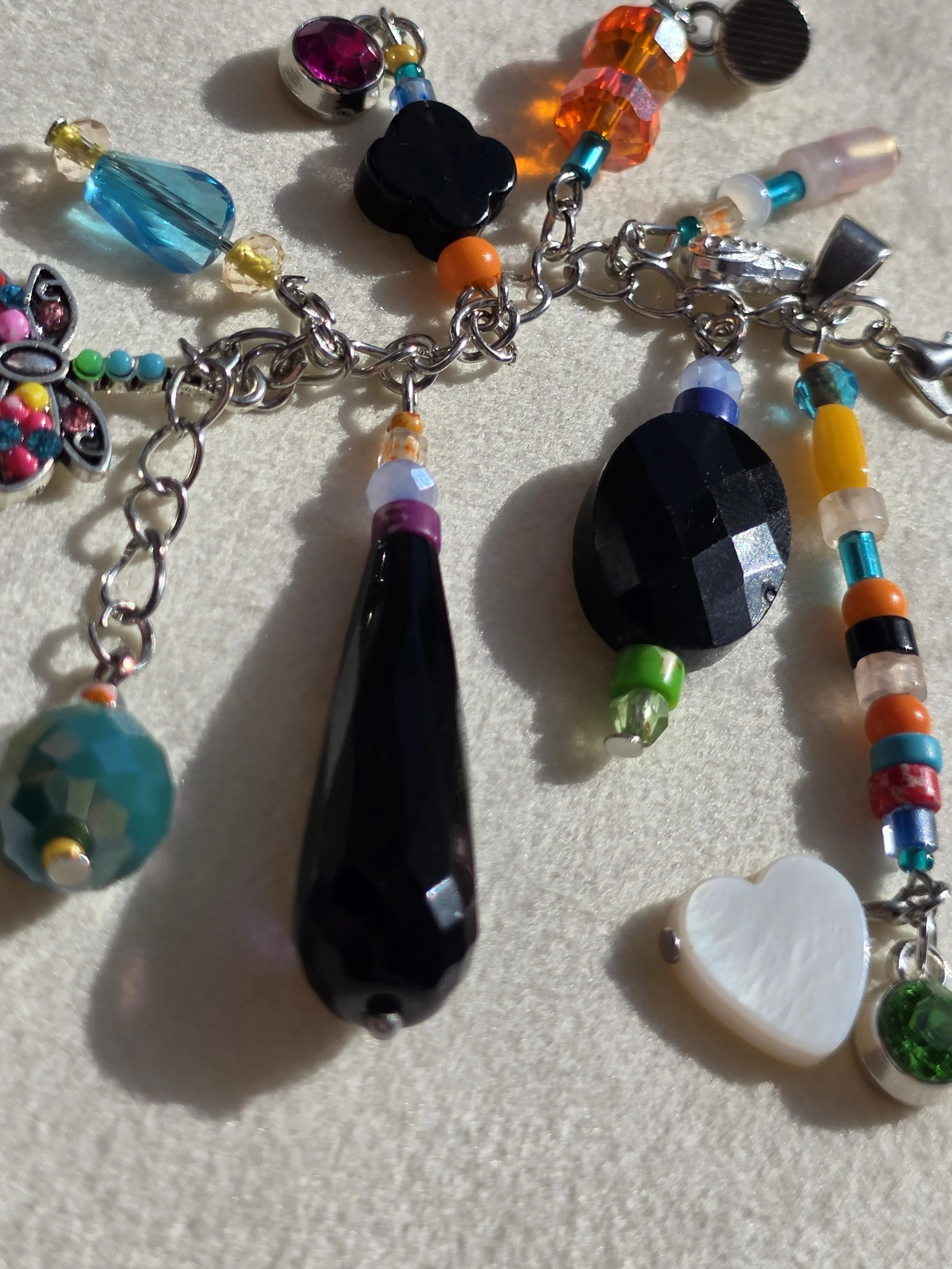 Close up of handmade bag charm with faceted black agate oval, black onyx teardrop and clover beads, and a colourful cascade of mixed gemstone and glass beads, lying flat