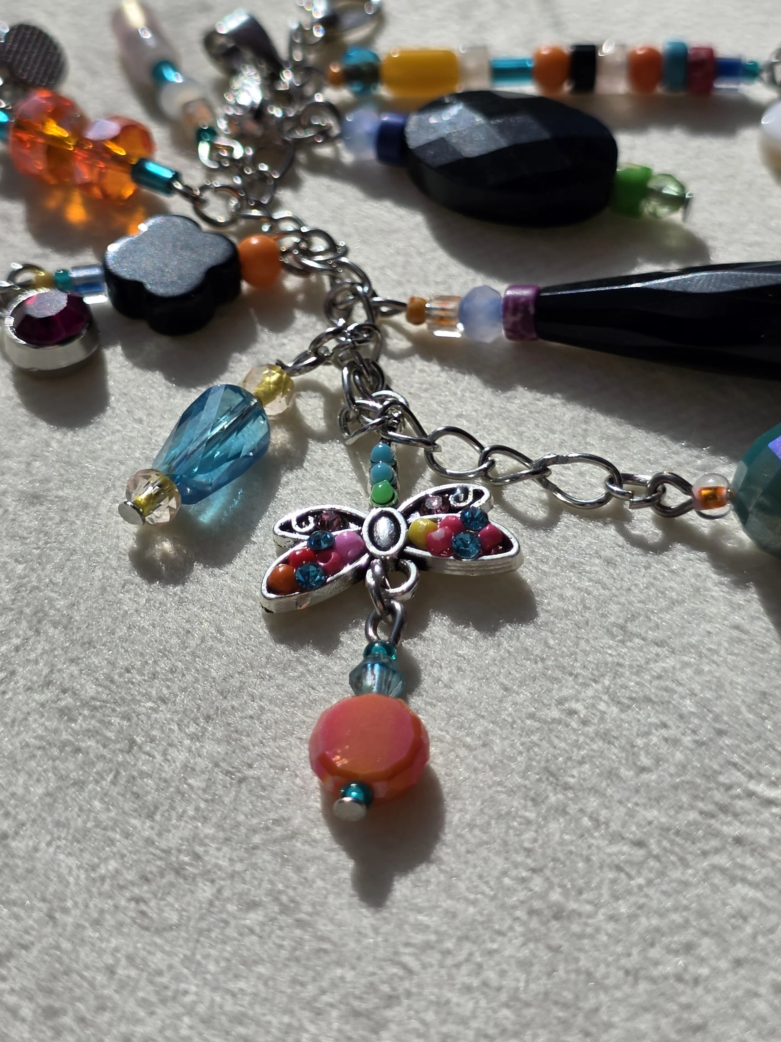 Close up of handmade bag charm with faceted black agate oval, black onyx teardrop and clover beads, and a colourful cascade of mixed gemstone and glass beads, lying flat