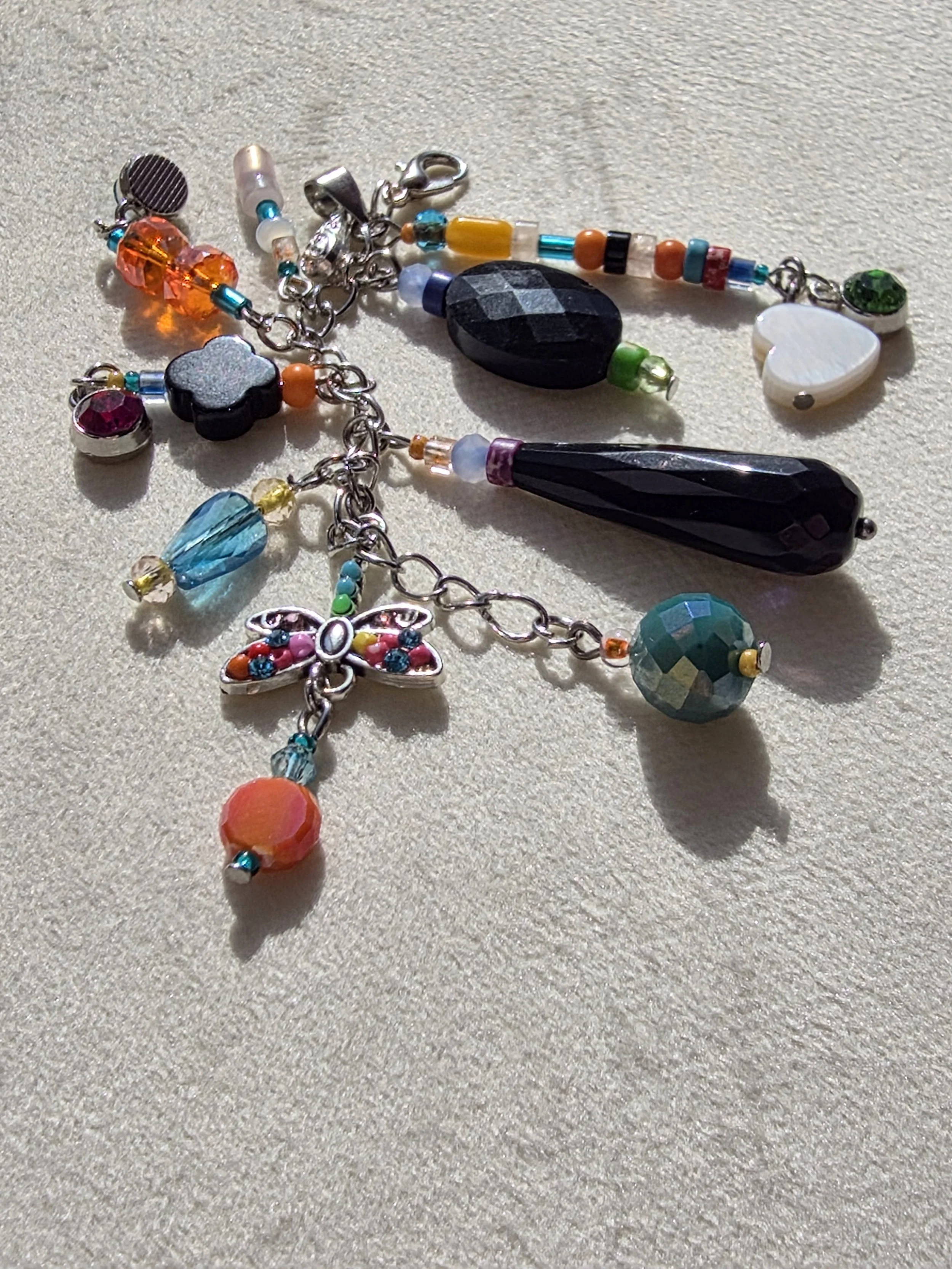 Handmade bag charm with faceted black agate oval, black onyx teardrop and clover beads, and a colourful cascade of mixed gemstone and glass beads, lying flat