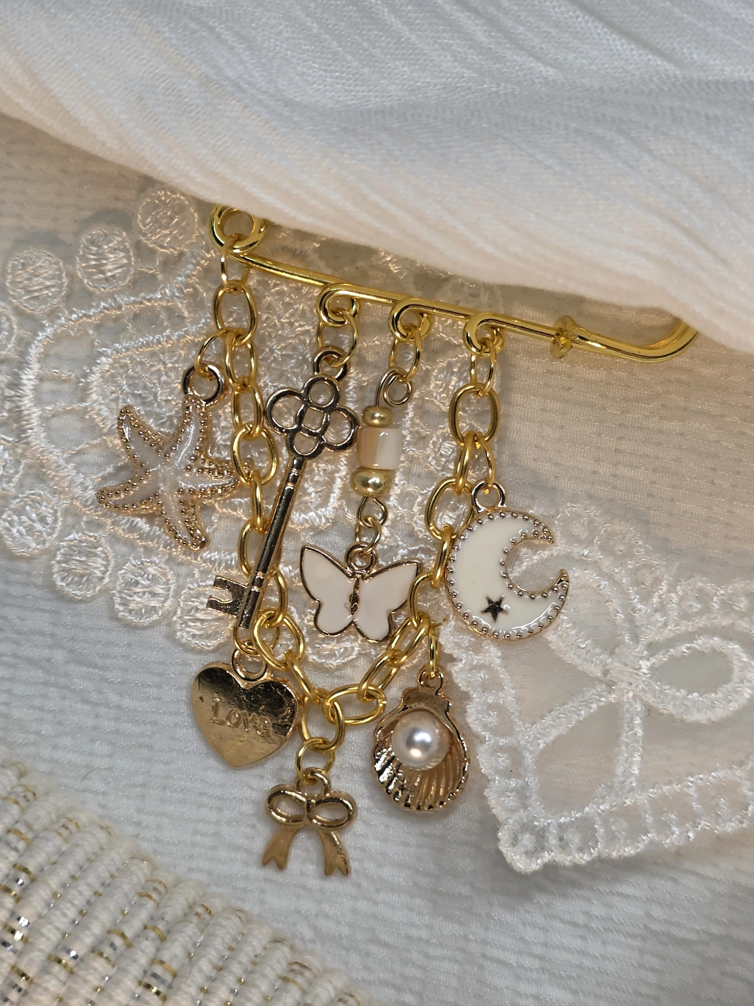 Gold-tone safety-pin brooch with a collection of charms including moon, shell, heart and starfish — The Maria by Charm & Delight