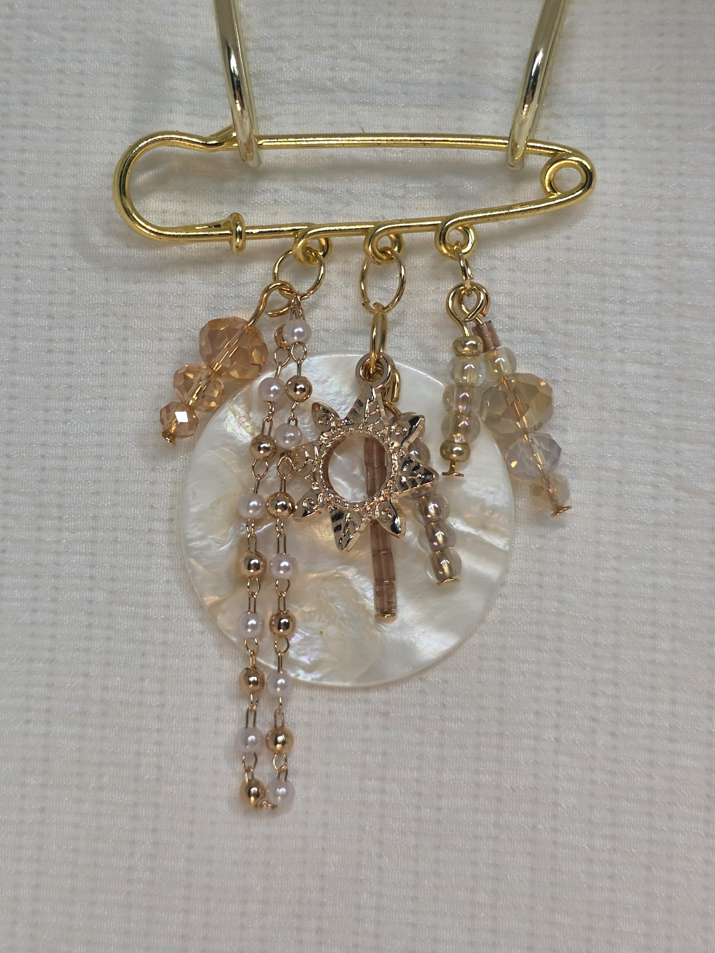Gold-tone safety-pin brooch with mother-of-pearl centre, sun charm and caramel glass dangles — The Soleil by Charm & Delight