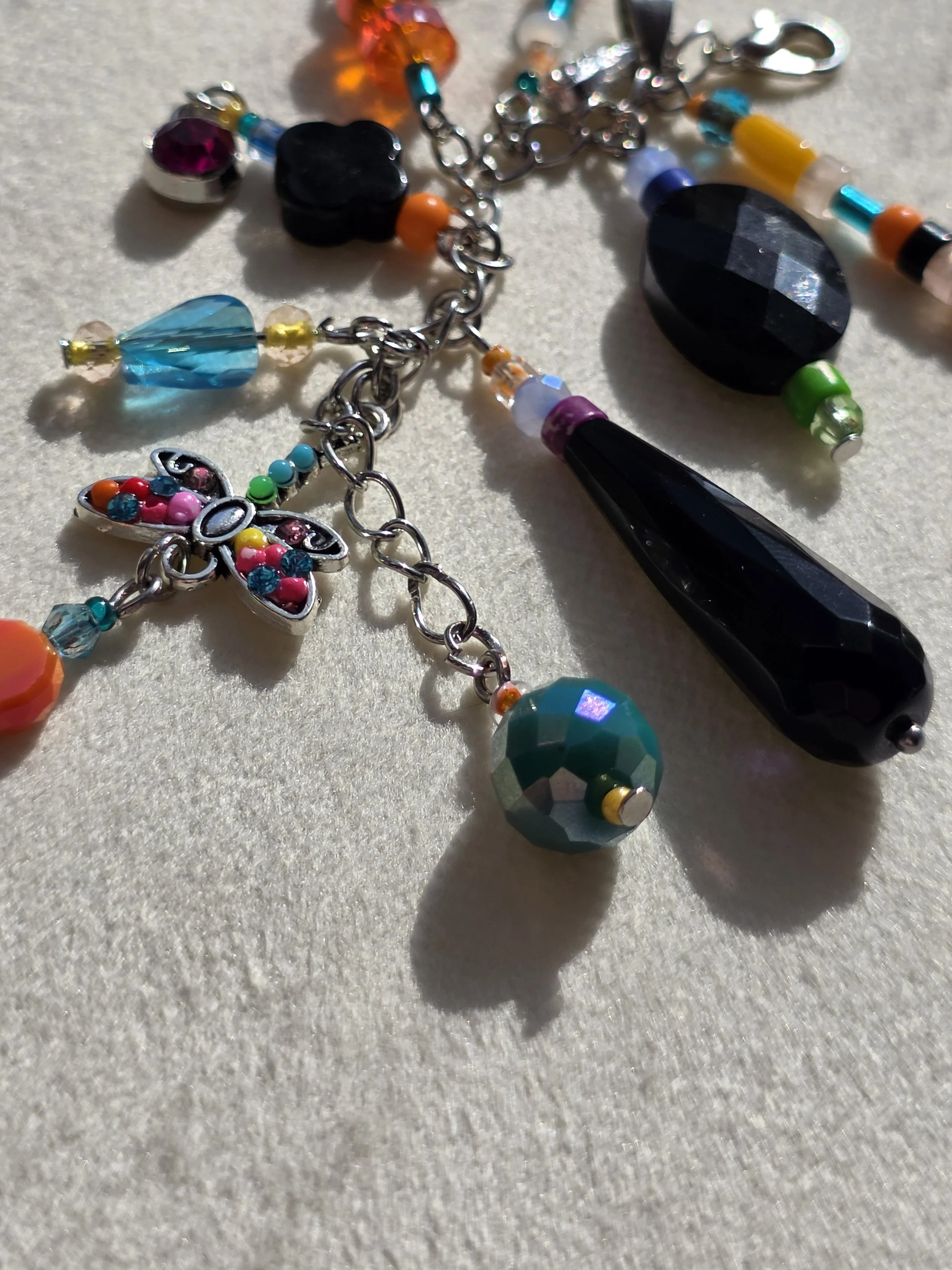 Close up of handmade bag charm with faceted black agate oval, black onyx teardrop and clover beads, and a colourful cascade of mixed gemstone and glass beads, lying flat