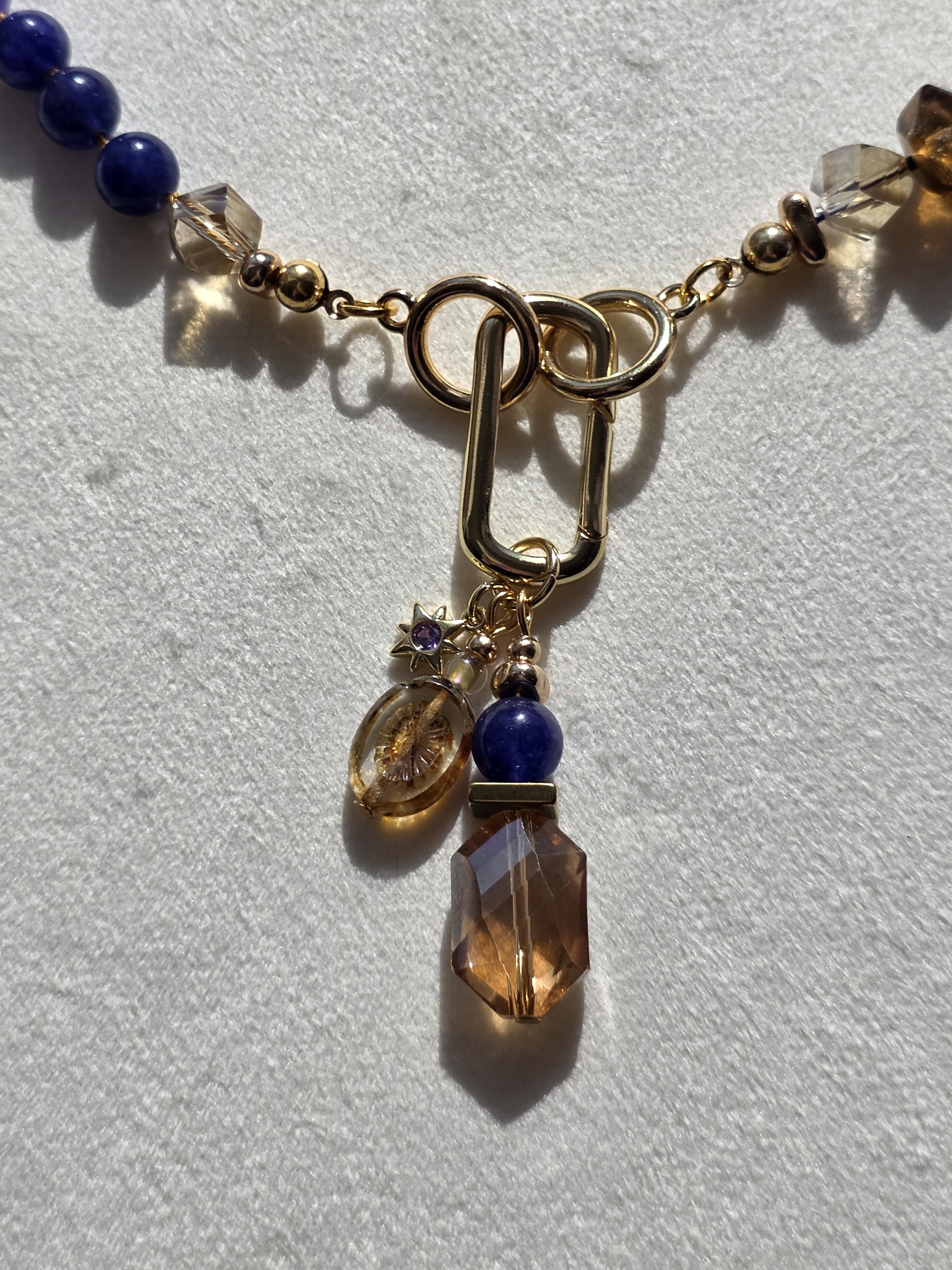 Close-up of charm cluster on The Vesper necklace featuring amber glass, quartzite, embossed glass bead and a small star charm