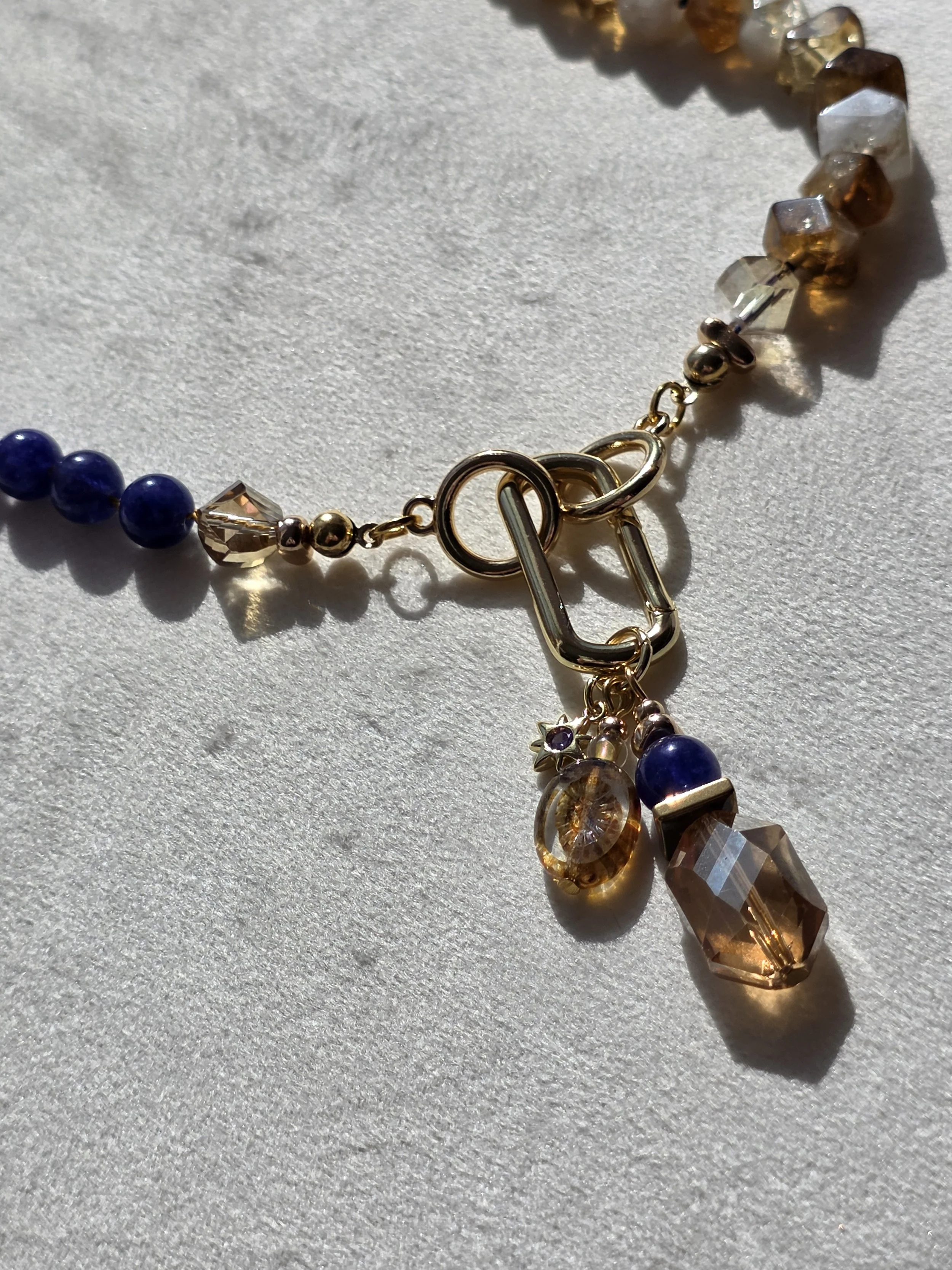 Close-up of charm cluster on The Vesper necklace featuring amber glass, quartzite, embossed glass bead and a small star charm