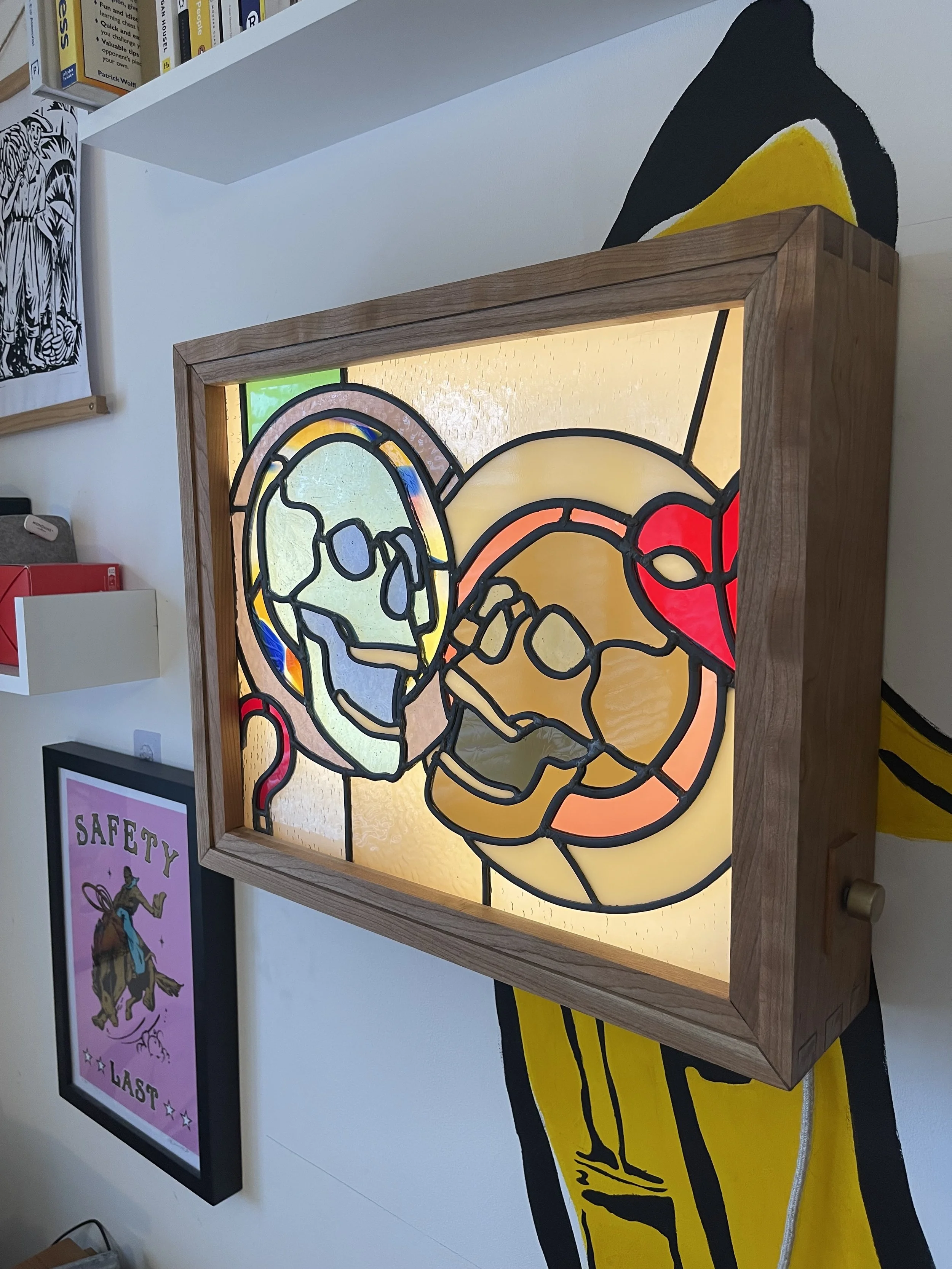 Decorative stained glass artwork depicting two hands clasped together, framed and illuminated from behind.