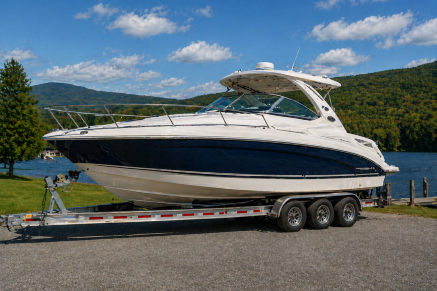 Blue-and-white cabin cruiser secured on a boat trailer beside a lake.