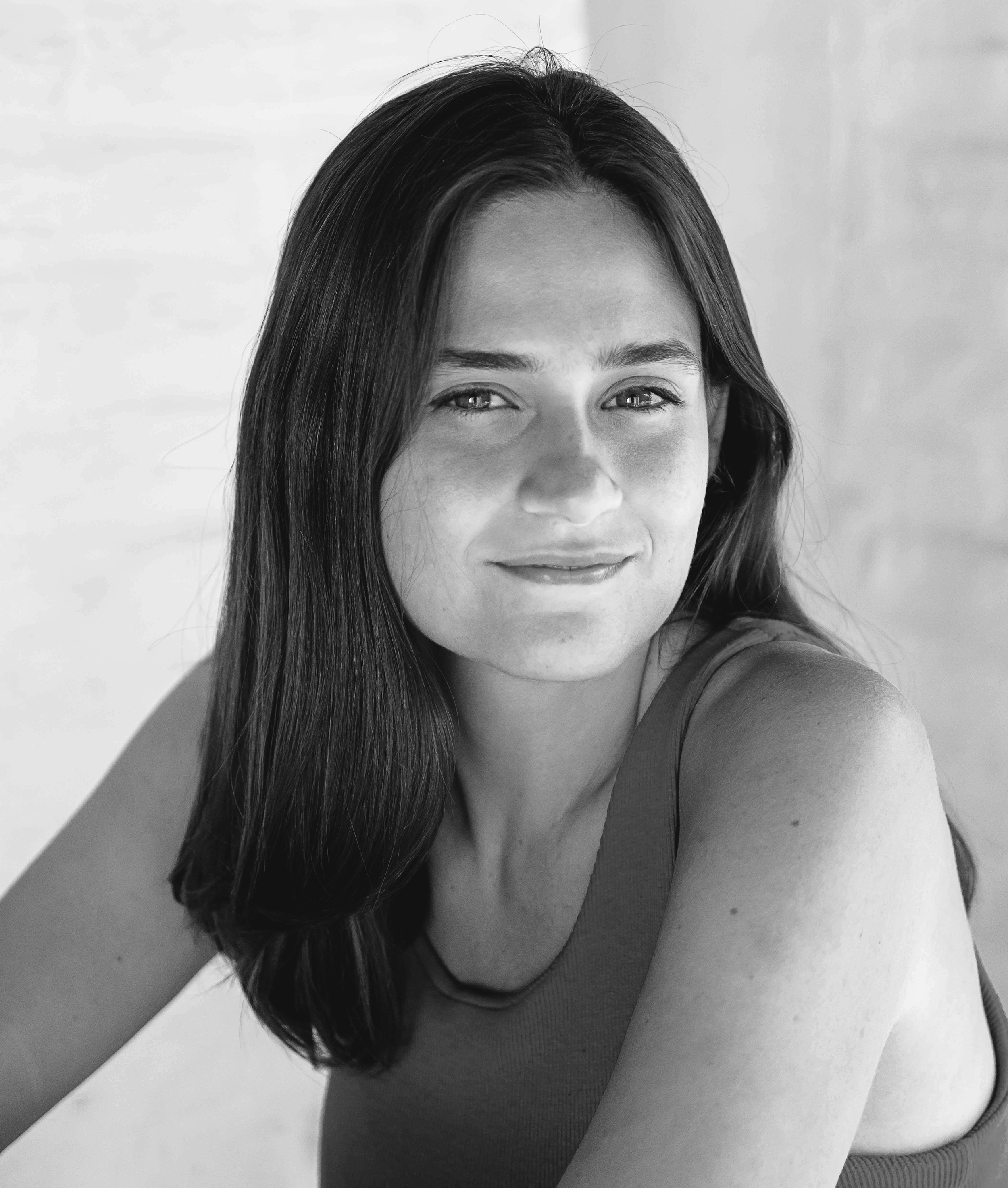 Close-up black and white photo of a woman with long dark hair smiling, wearing a sleeveless top.
