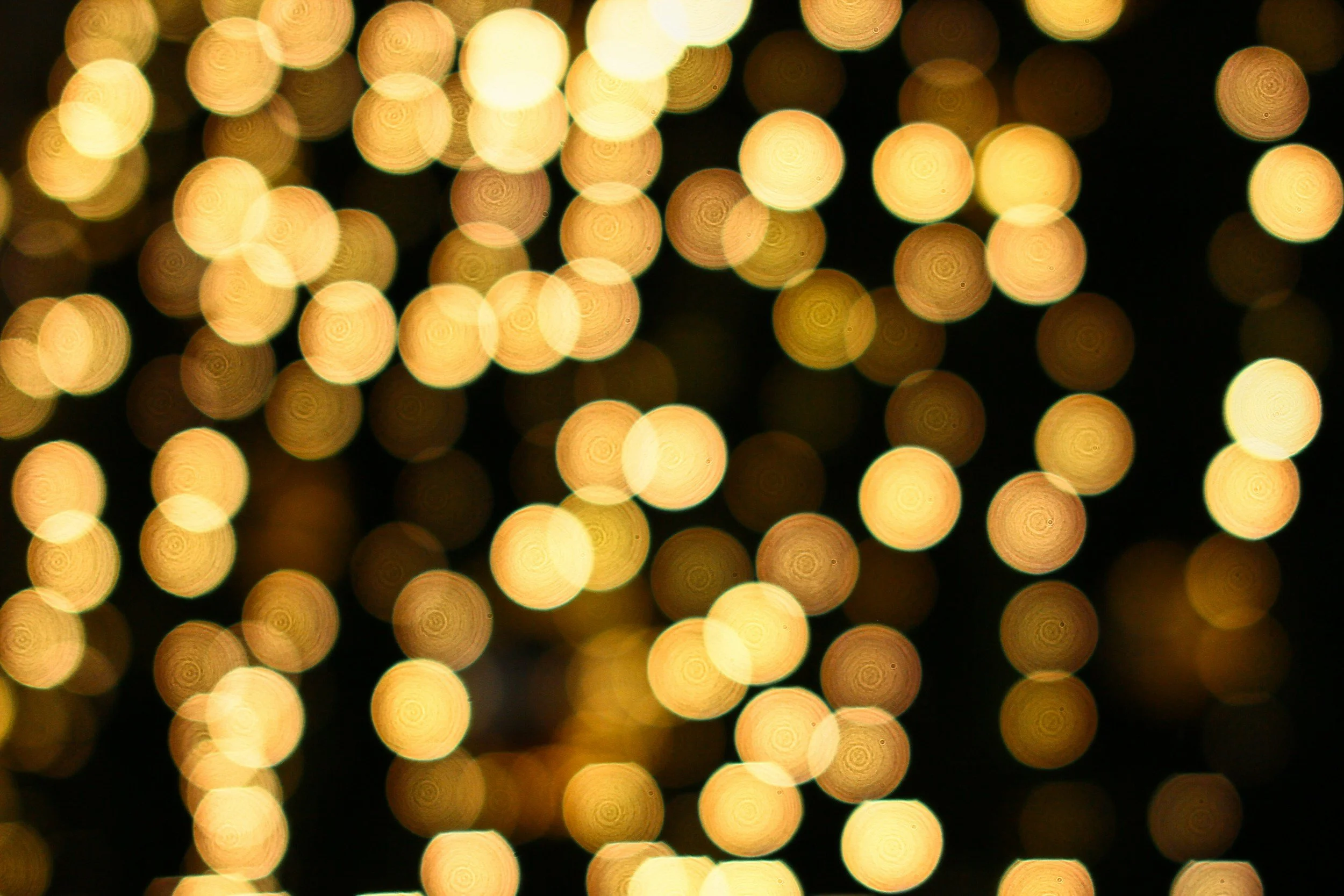 Blurred image of numerous yellow and gold lights, creating a bokeh effect against a dark background.