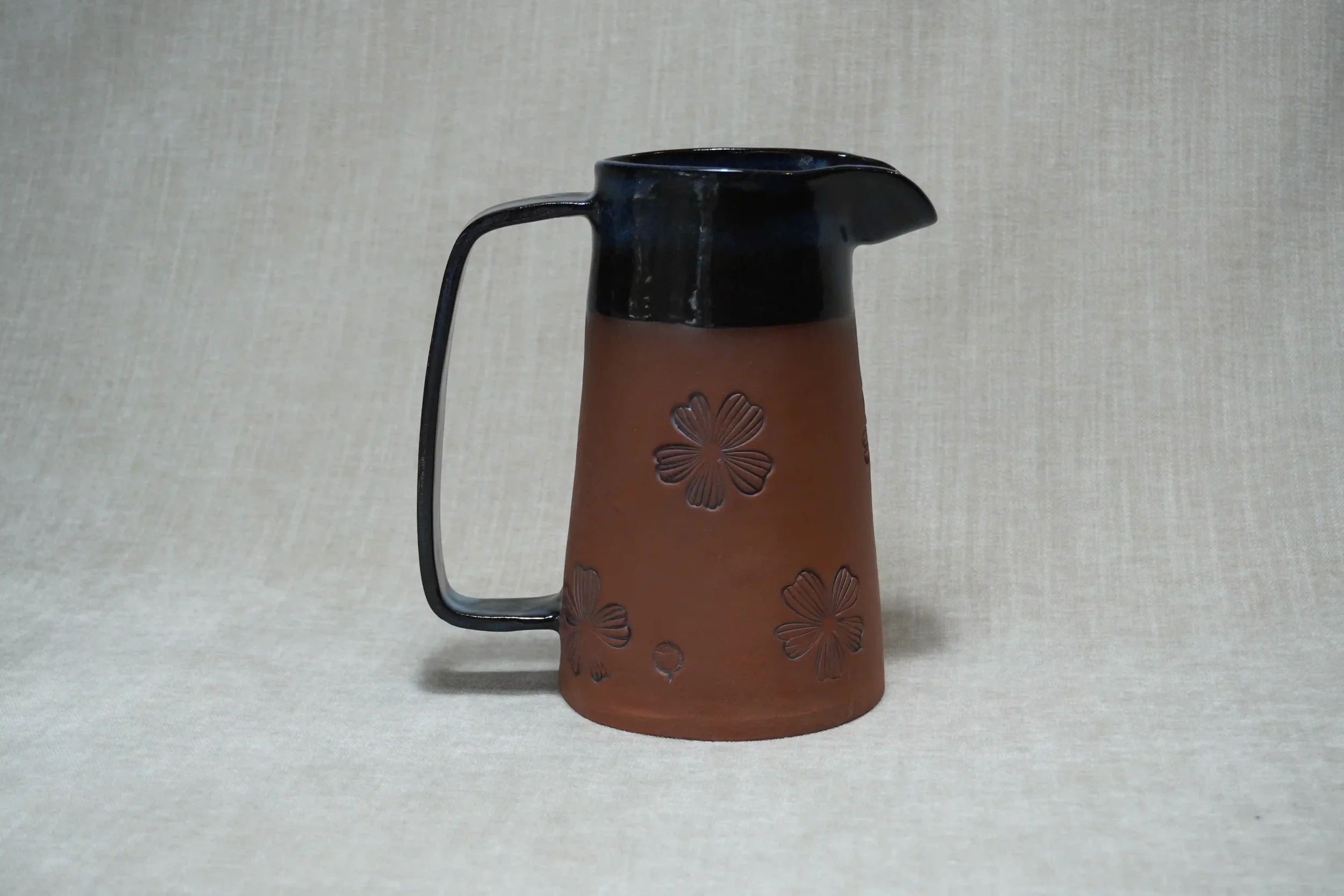	
Brown ceramic terracotta pitcher (jug) with black glaze upper and handle, decorated with floral motif.