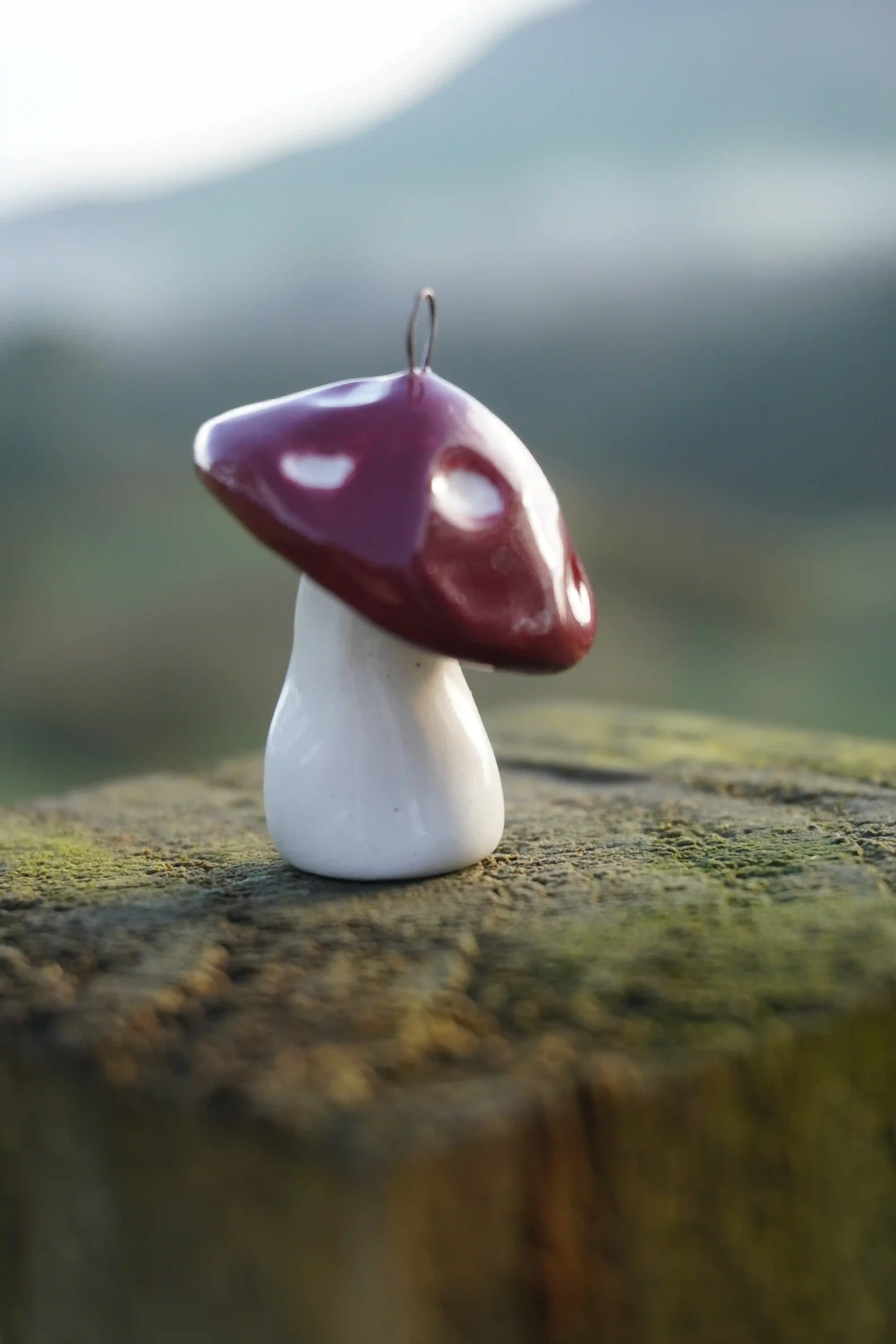 A small ceramic mushroom with a shiny purple cap and a white stem displayed on a piece of wood outdoors.