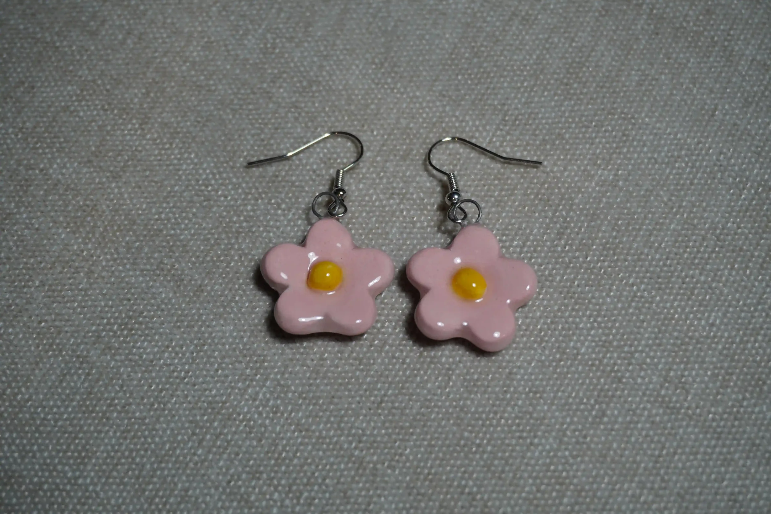 Pair of ceramic pottery pink flower-shaped earrings with yellow centers on a gray textured background.