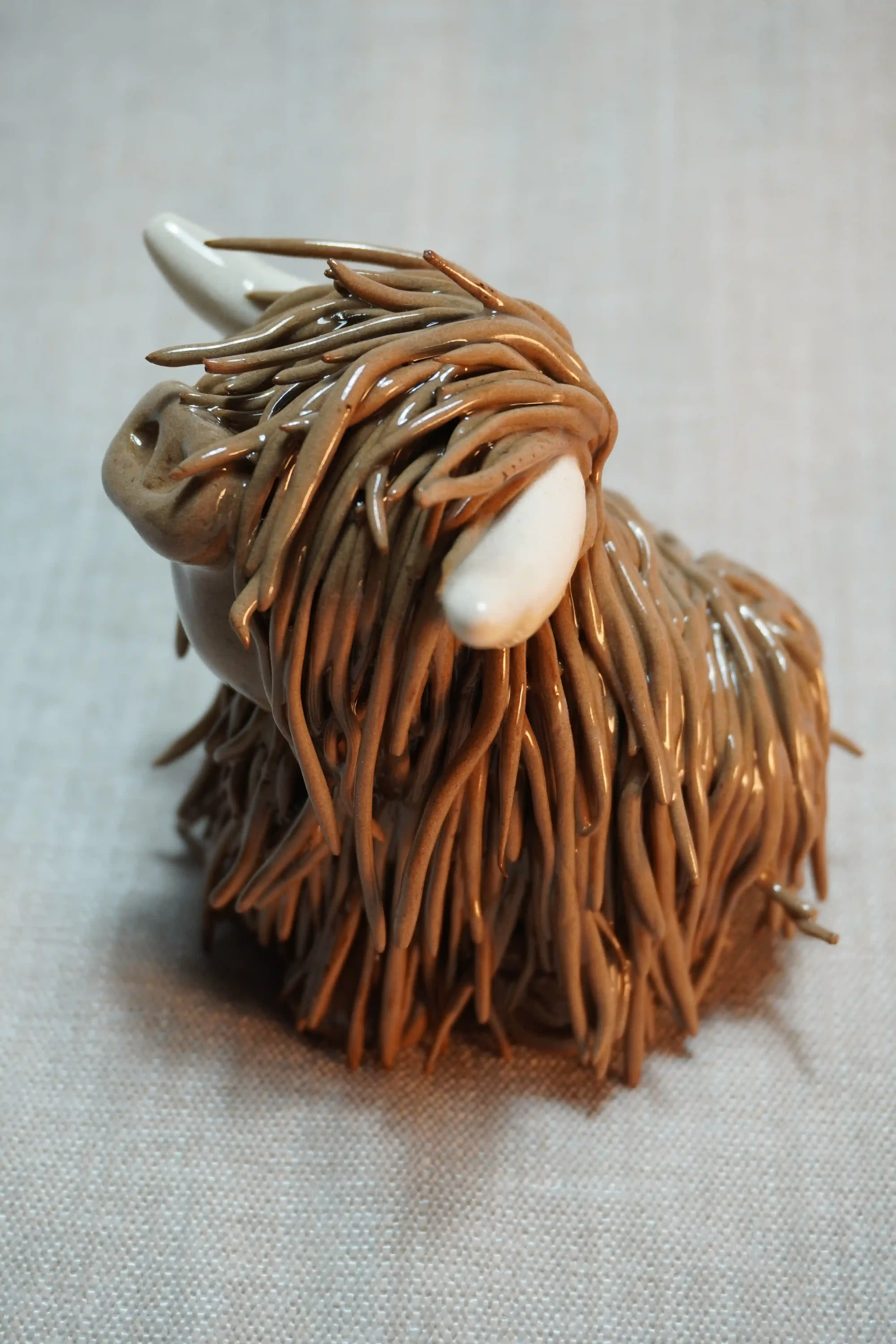 Side view of a medium brown handmade ceramic ornament of a Highland Cow with beige horns.