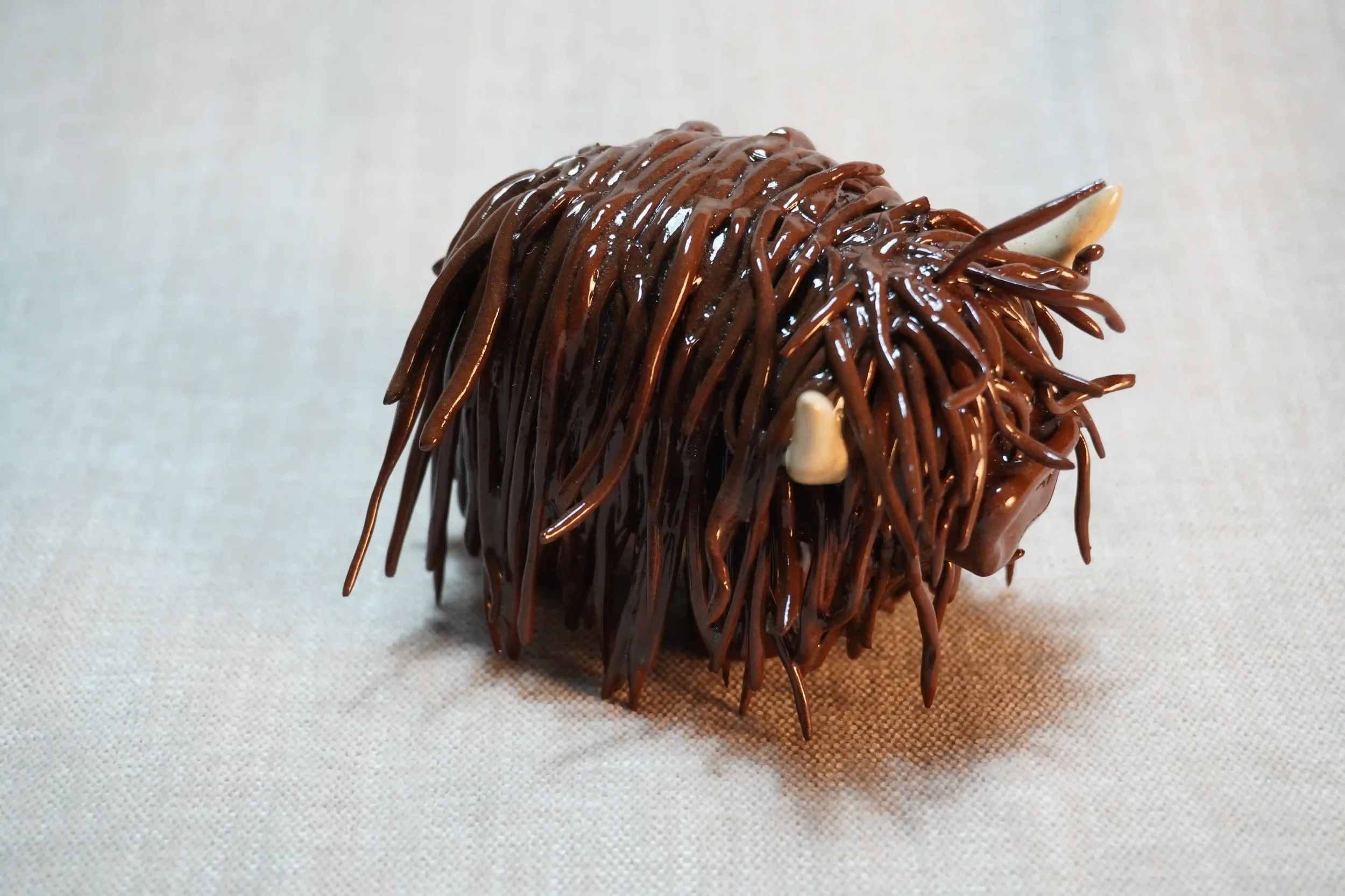 	
Quarter front view of a ceramic sculpture of a Highland Cow ornament with dark brown-coloured hair and beige horns.