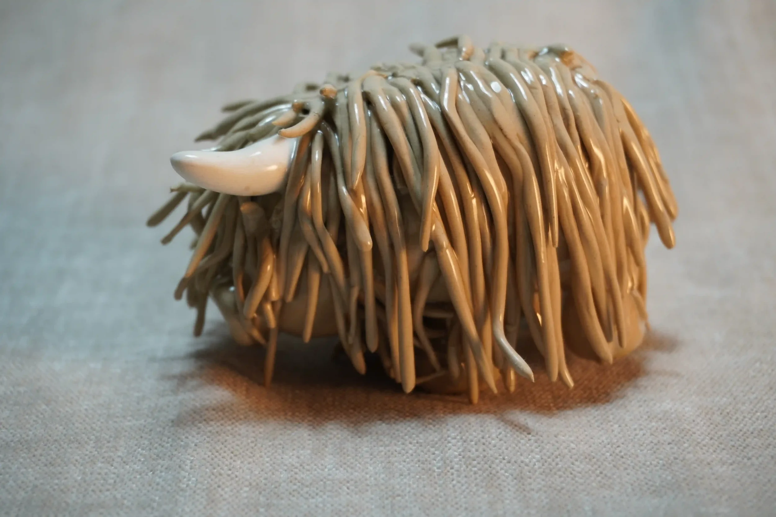 	
Side view of a handmade ceramic Highland Cow ornament with brown-coloured hair and beige horns.