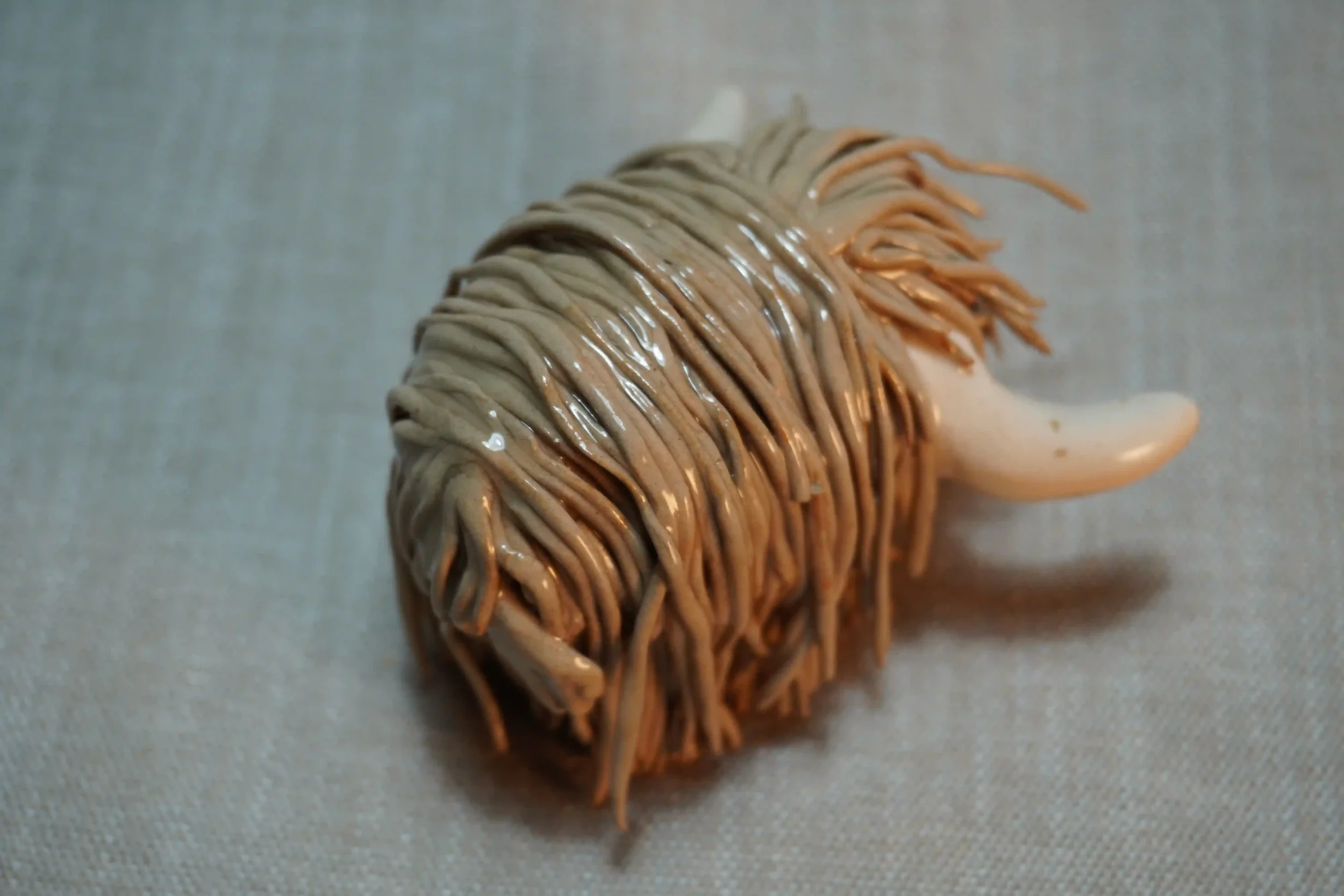Rear view of a handmade pottery ceramic sculpture of a Highland Cow ornament with light brown-coloured hair and beige horns.