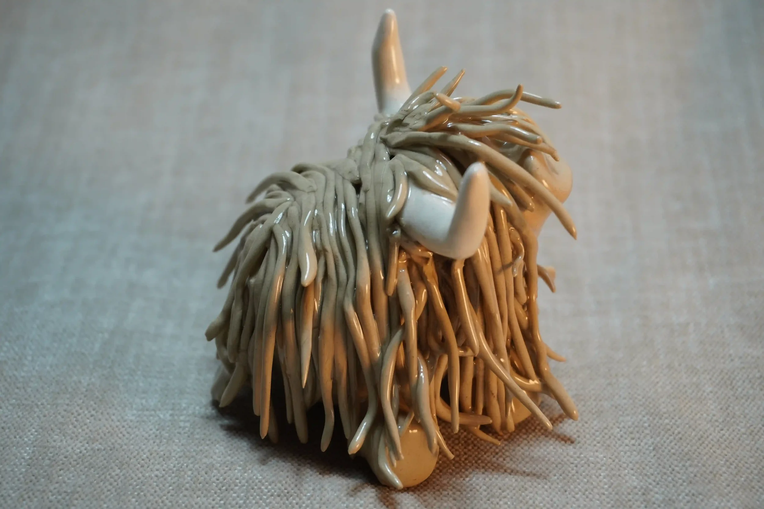 Side view of a ceramic sculpture of a Highland Cow ornament with light brown-coloured hair and curving beige horns.