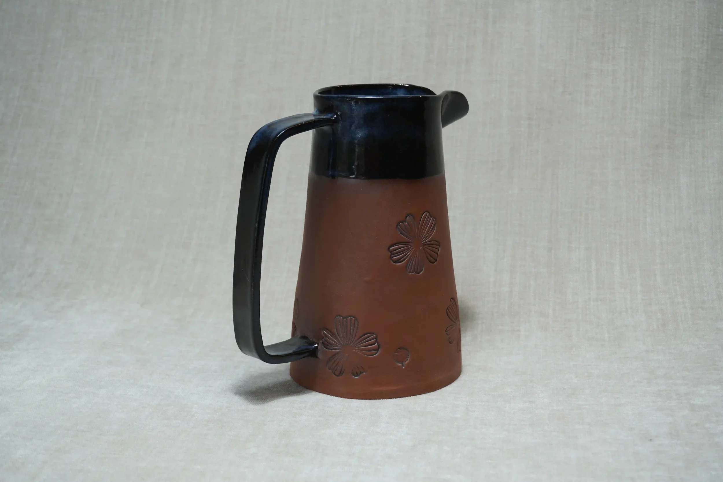 	
Handmade brown terracotta pitcher (jug) with black glaze upper and handle, decorated with floral motif.