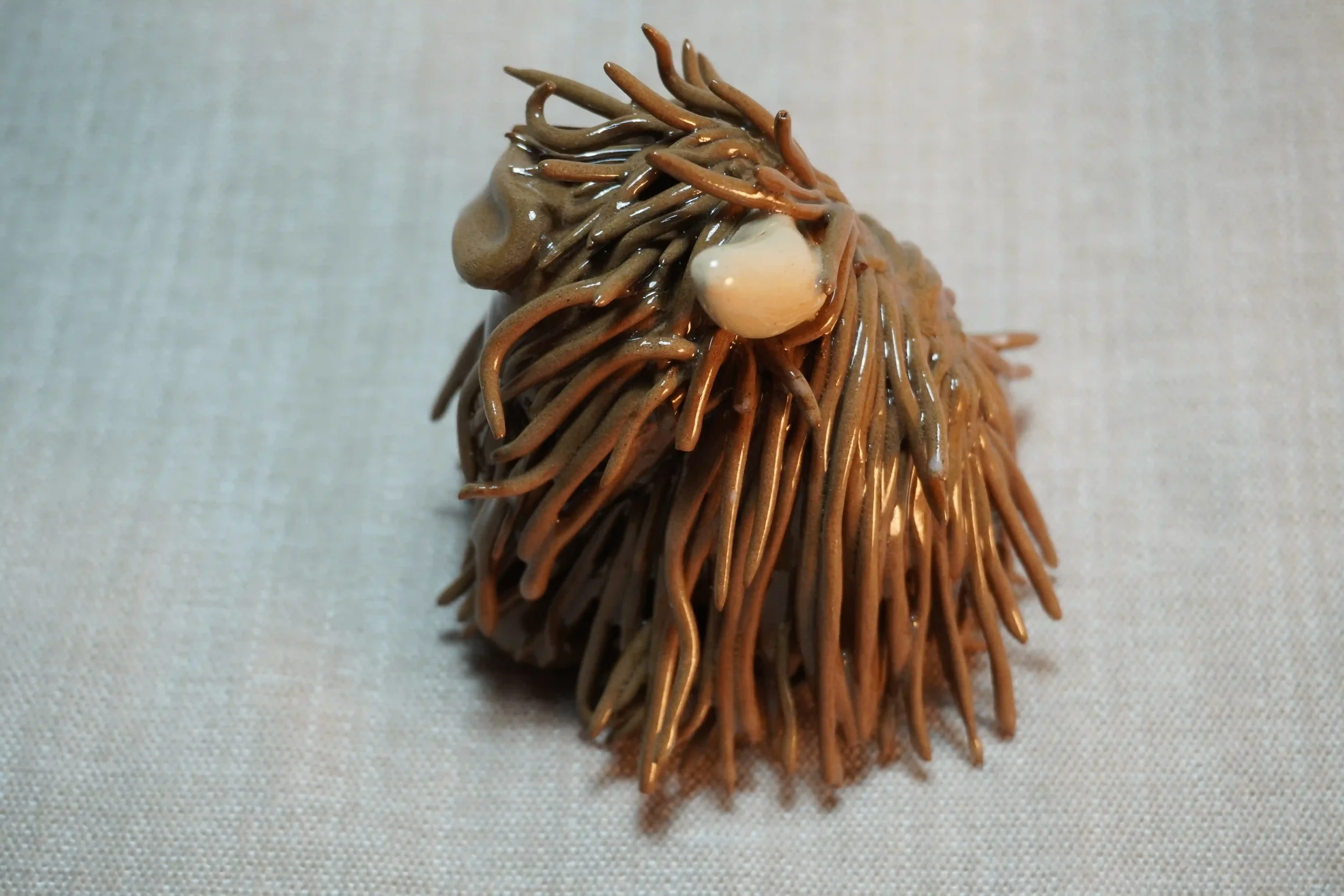 Side view of a handmade pottery ceramic sculpture of a cute Highland Cow ornament with milk chocolate-coloured hair and beige horns.